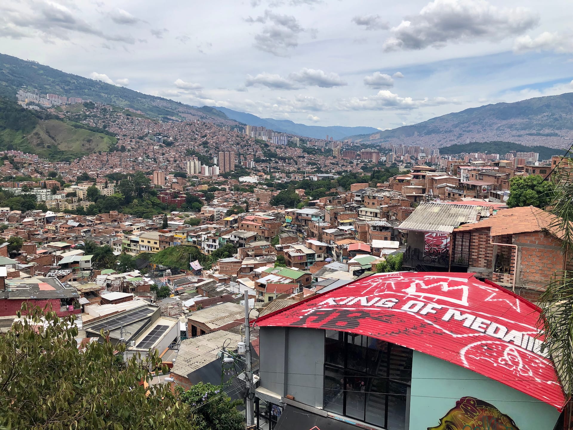 Medellín, Colombia Panoramic view of Medellín's expansive cityscape, revealing the intricate patchwork of brick houses climbing steep hillsides, with modern high-rise buildings and lush mountains in the background.