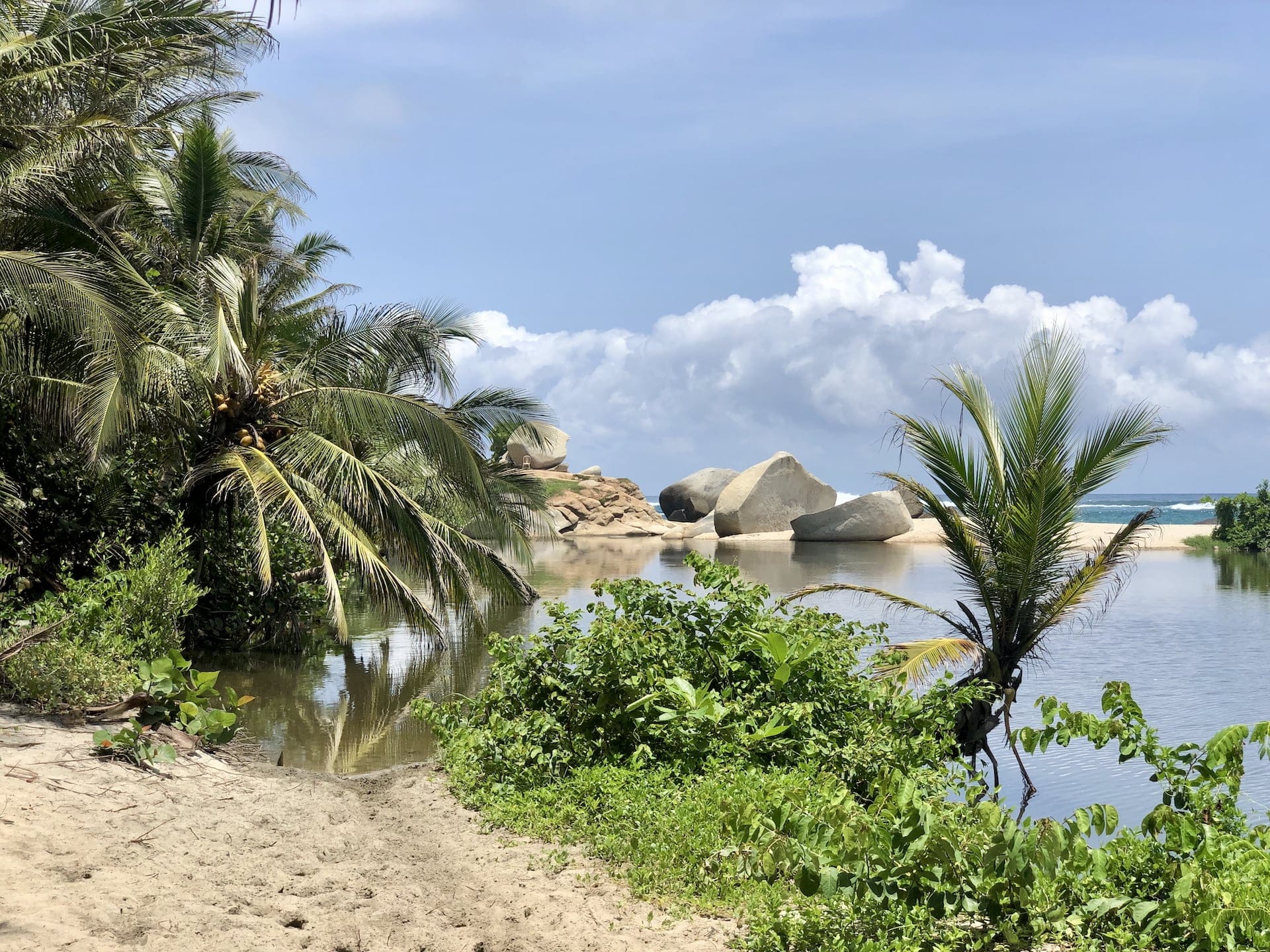 Tayrona National Park, Colombia A tranquil natural pool formed between massive rocks and palm trees, where the ocean meets the shore.