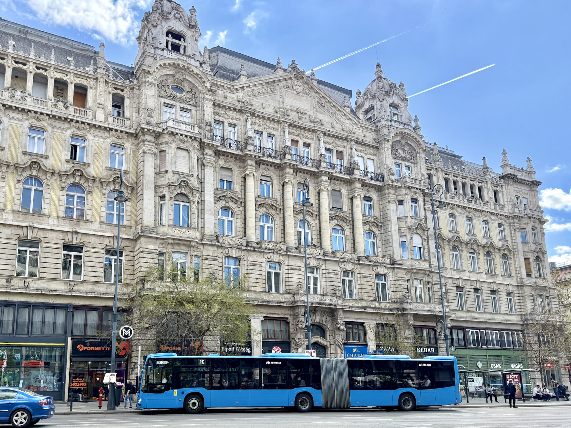 Articulated bus in front of a historic building. The "M" sign marking the metro station is also visible.