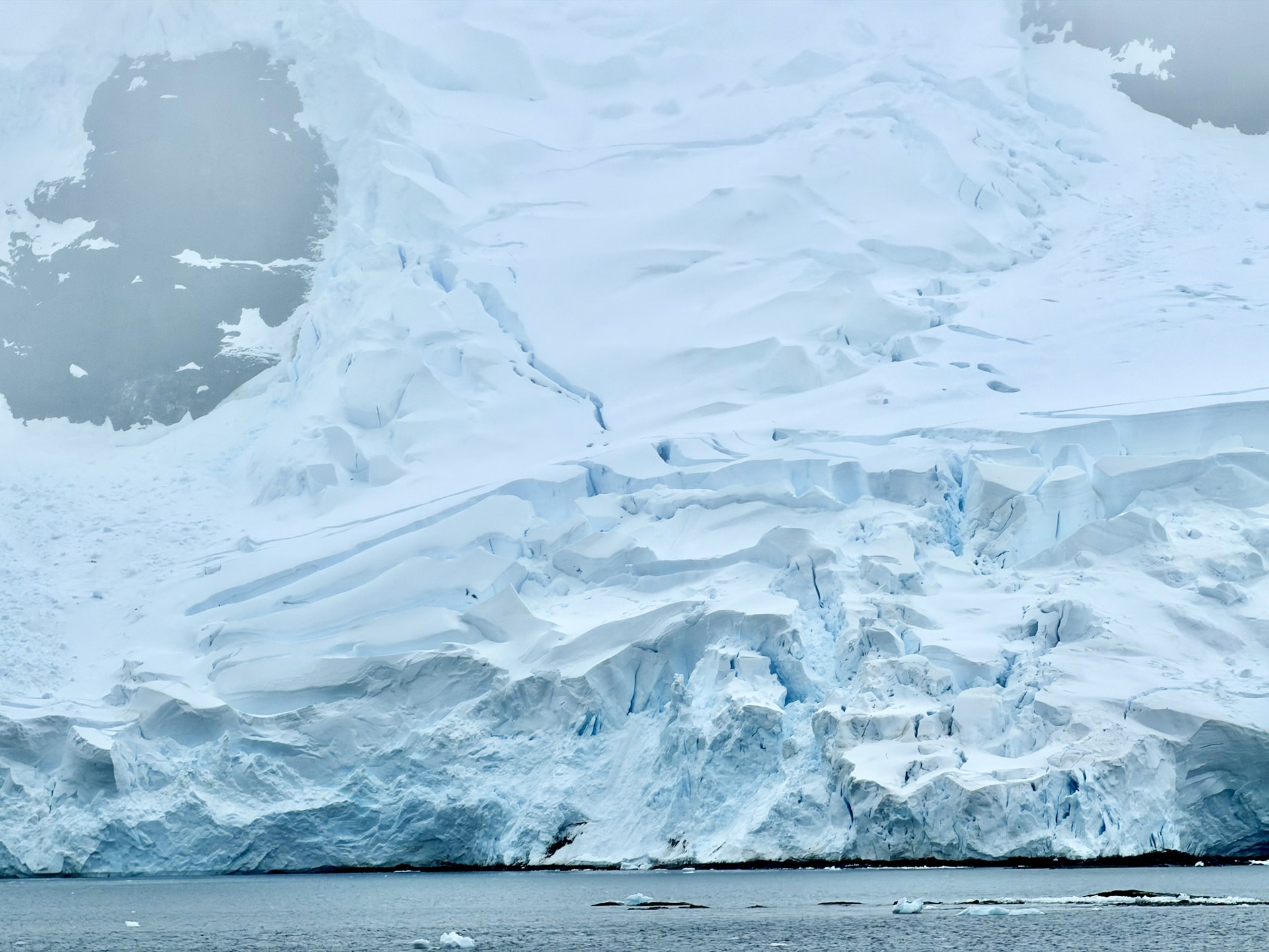 Large glacier with deep crevasses descending from snow-covered mountains into the dark waters near Trinity Island, Antarctica.