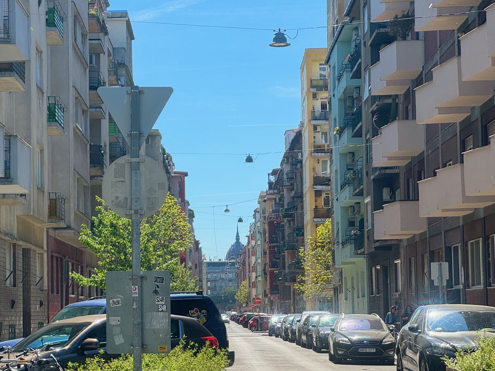 Long street view in Újlipótváros Budapest showing uniform apartment building heights with the Hungarian Parliament dome visible in the distance