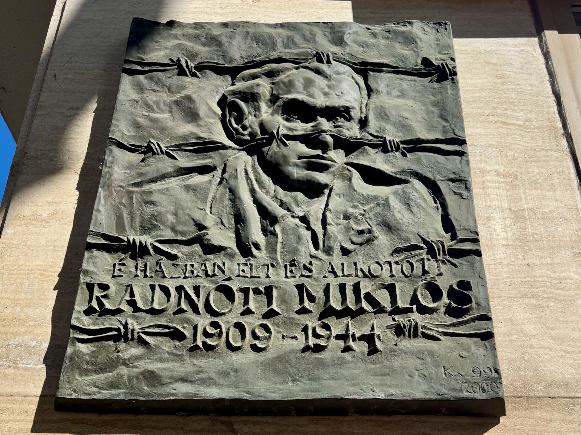 Bronze memorial relief plaque for poet Radnóti Miklós showing face behind barbed wire on building in Budapest