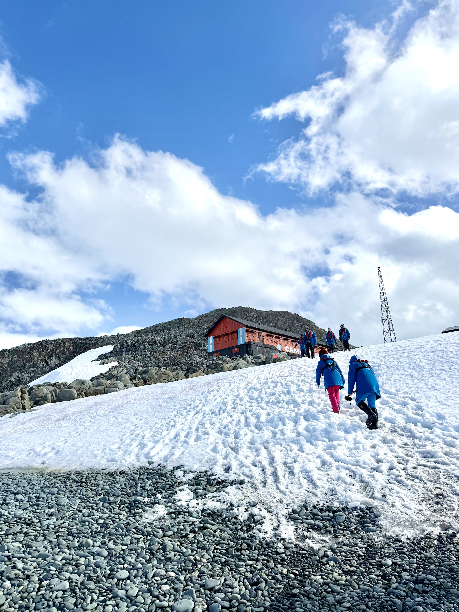 Antarctic expedition cruise passengers in blue parkas walking uphill toward Cámara Station on Half Moon Island