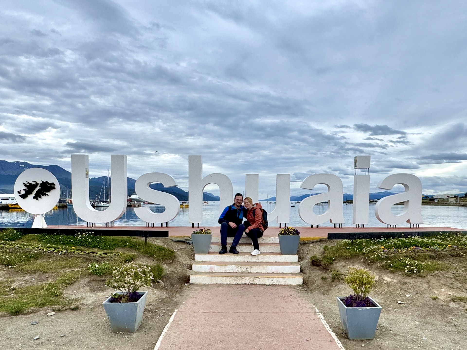 Couple at Ushuaia sign Beagle Channel Tierra del Fuego Argentina László and Andrea posing at the Ushuaia city sign with the Beagle Channel harbor and mountains behind, Tierra del Fuego, Argentina