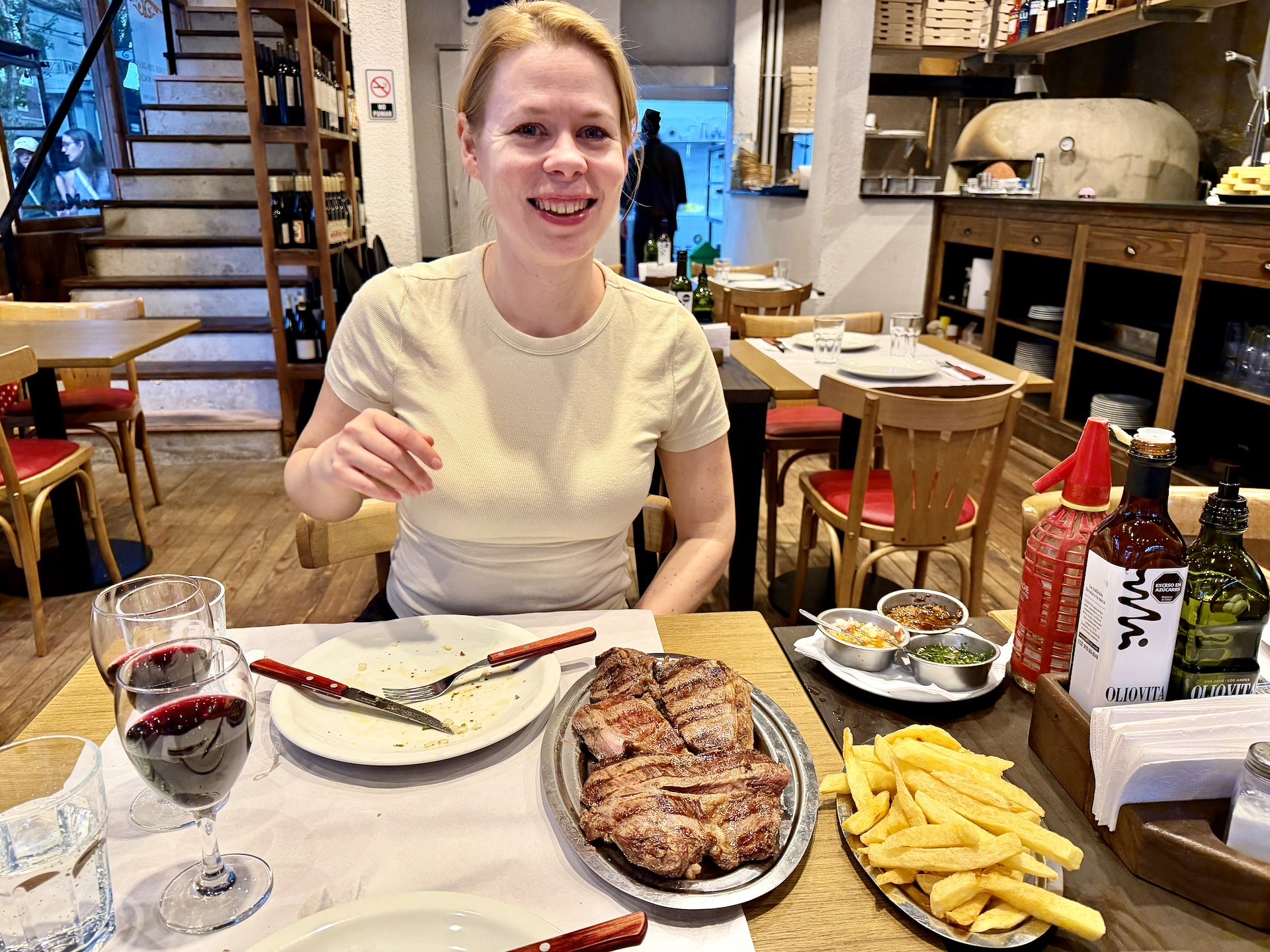 Steak platter at Buenos Aires parrilla Argentina Andrea at a Buenos Aires parrilla with a large grilled steak platter, fries, chimichurri, and a glass of red wine on the table