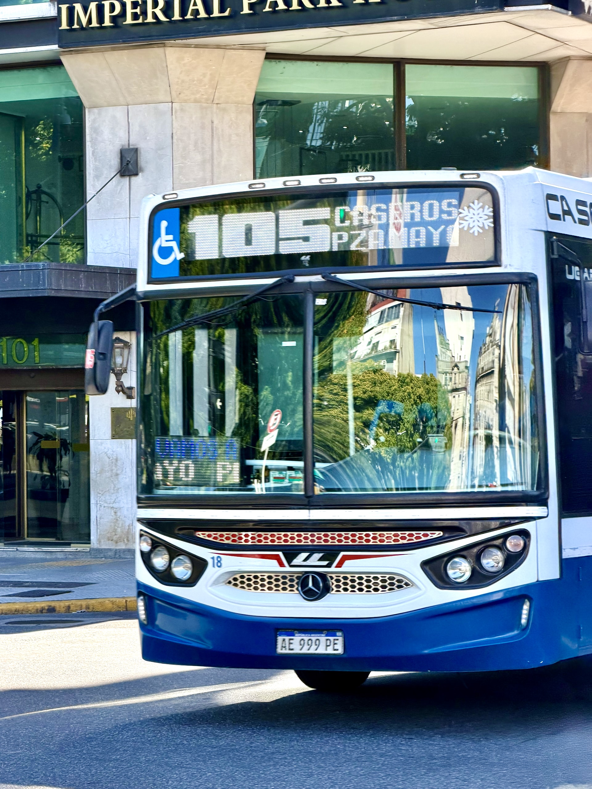 A white and blue colectivo bus on line 105 passing the Imperial Park Hotel in Buenos Aires.