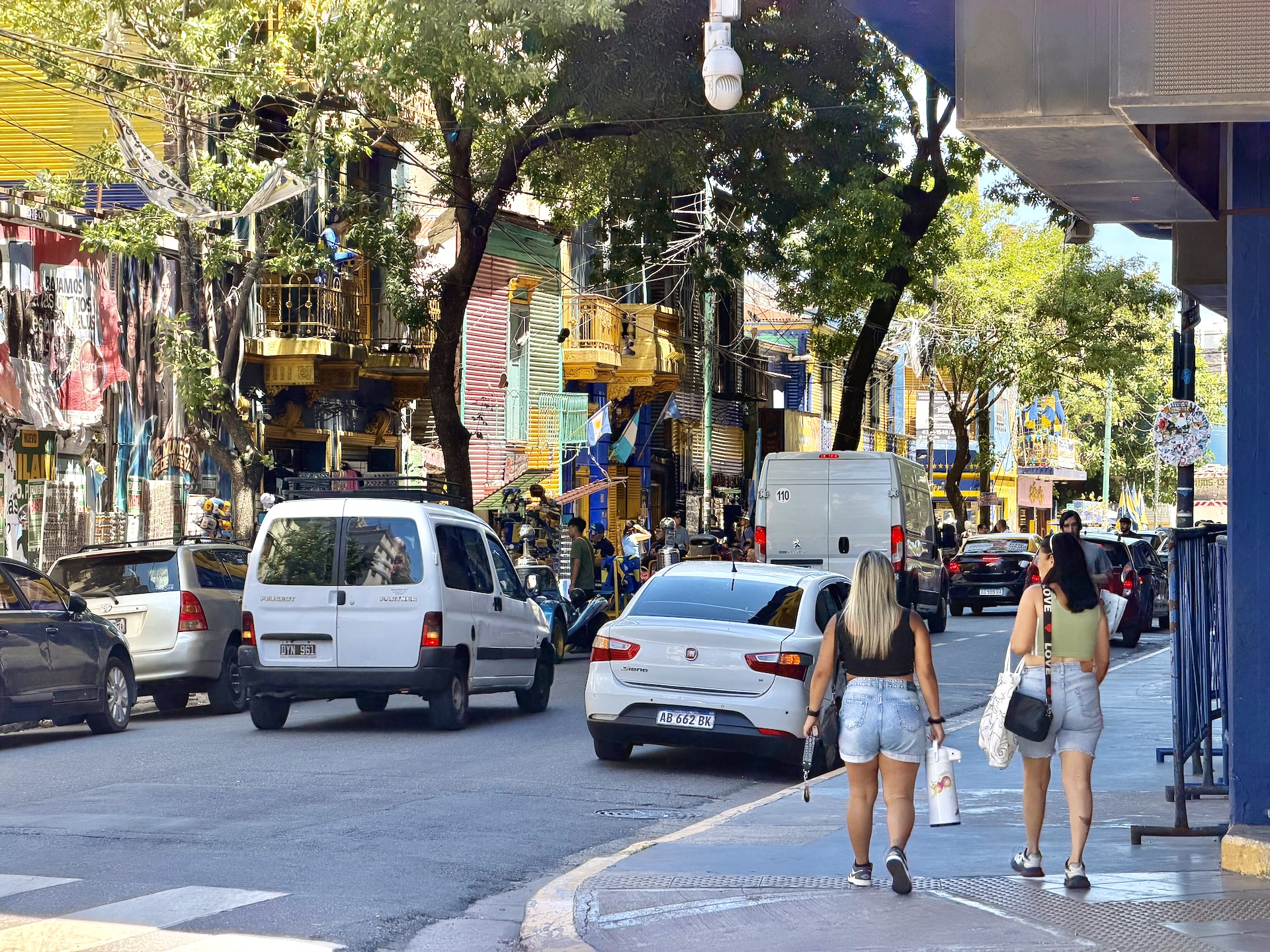 A colorful street in the La Boca neighborhood of Buenos Aires, with painted buildings, cars, and pedestrians.