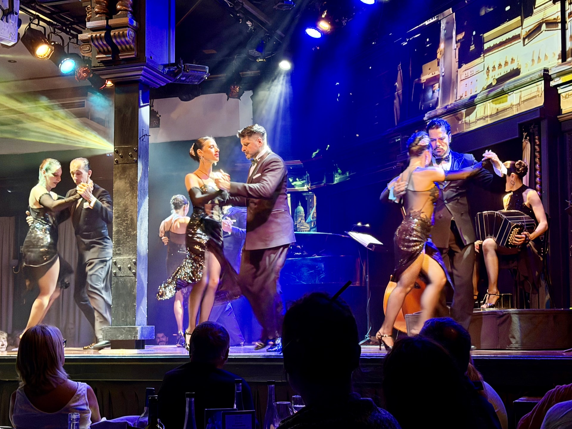 Three couples performing on stage during a tango show, with a bandoneón player, at El Querandí in Buenos Aires.