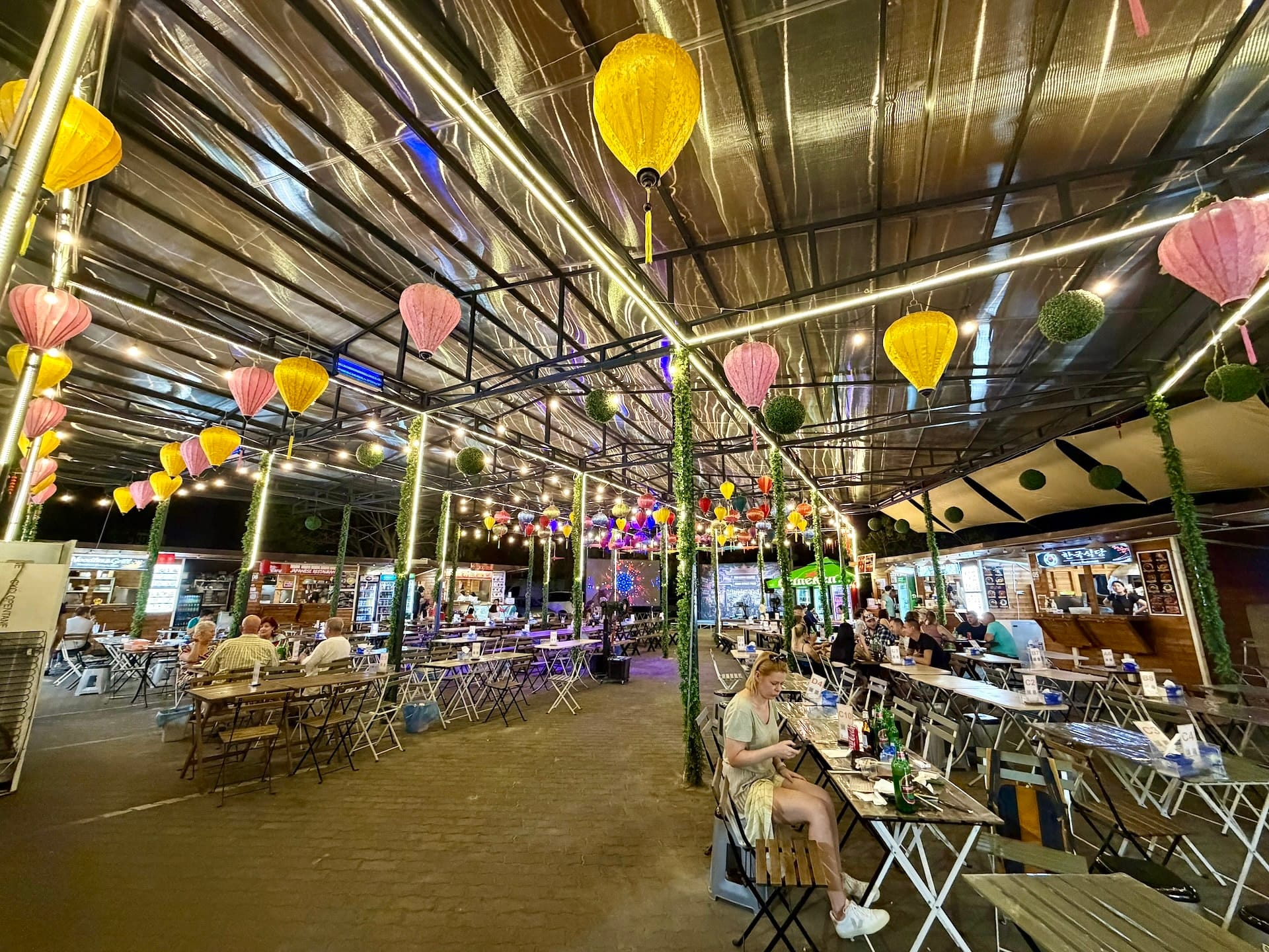 Bian Garden Budapest lit up in the evening Bian Garden at night with lit lanterns and LED strips, a woman checking her phone at a table