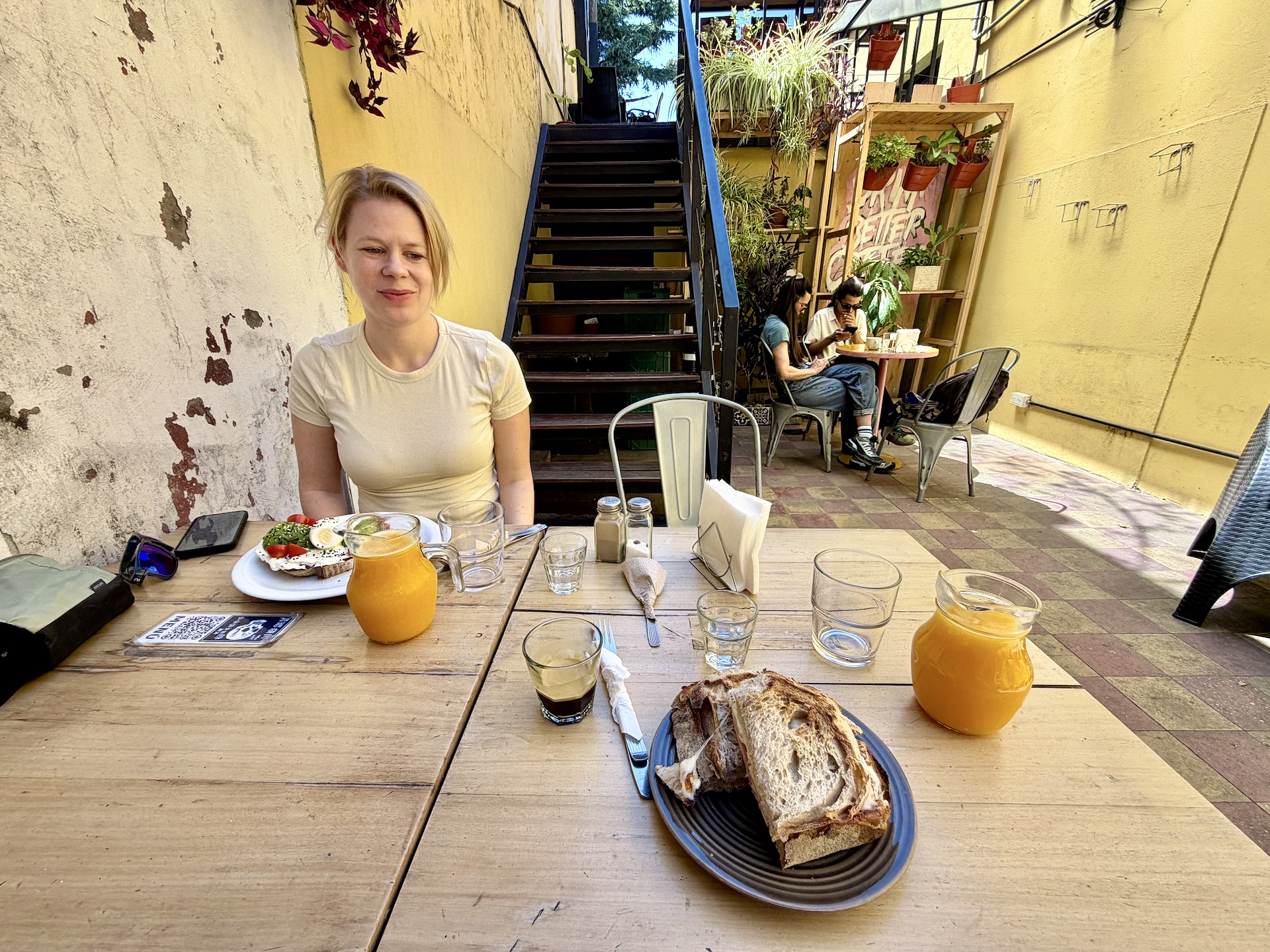 Breakfast at Full City Coffee Roasters in Palermo, Buenos Aires Andrea at a café table in a plant-filled courtyard in Palermo, a breakfast of bread, coffee, and fresh juice in front of her.
