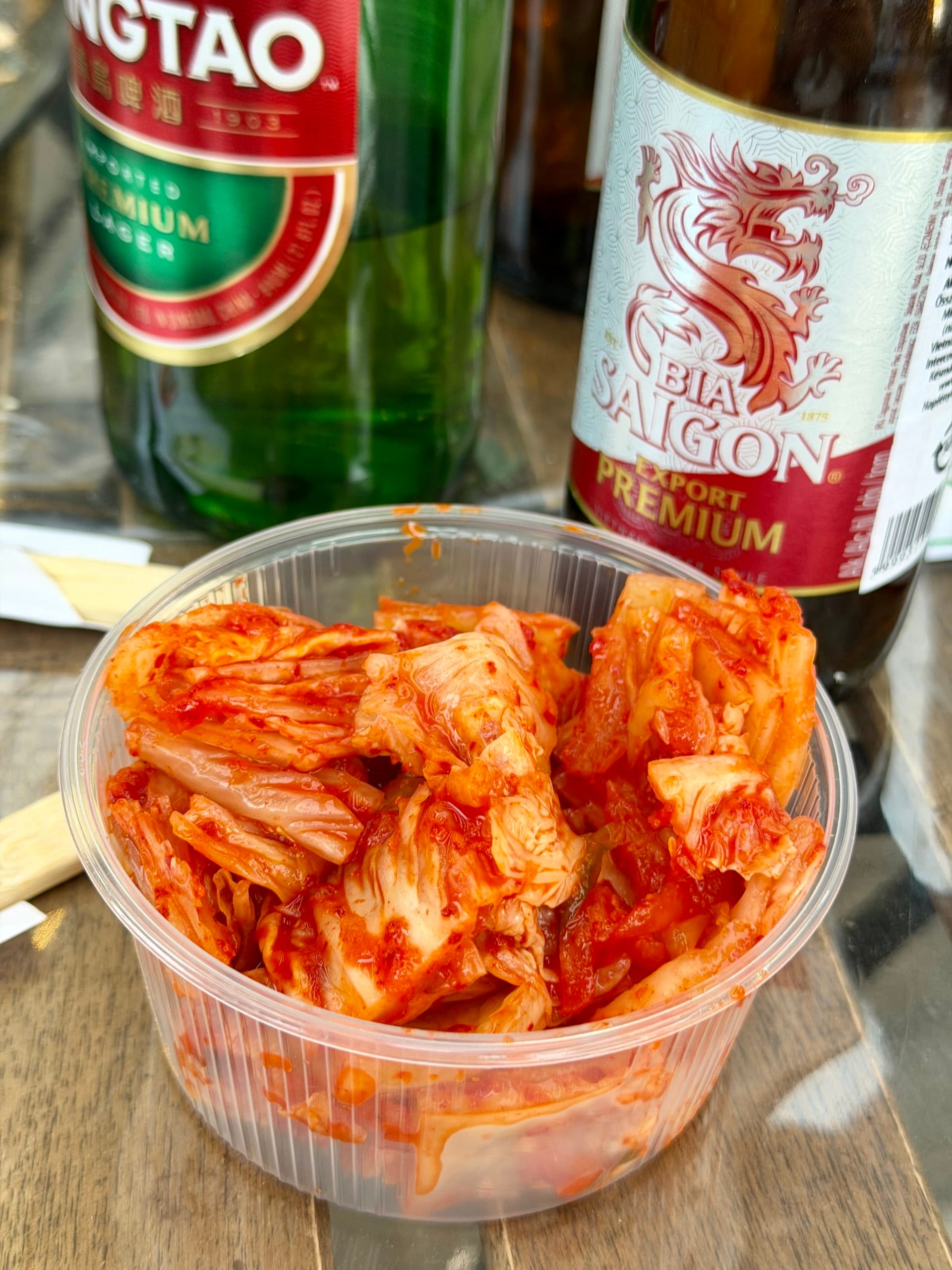 Kimchi with Tsingtao and Bia Saigon beer at Bian Garden Plastic container of kimchi on a wooden table between bottles of Tsingtao and Bia Saigon beer