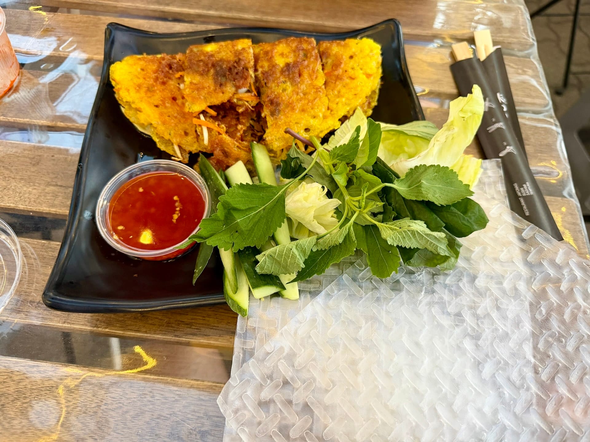 Vietnamese bánh xèo pancake at Bian Garden Budapest Crispy Vietnamese bánh xèo pancake on a black plate with fresh herbs, cucumber, dipping sauce and rice paper
