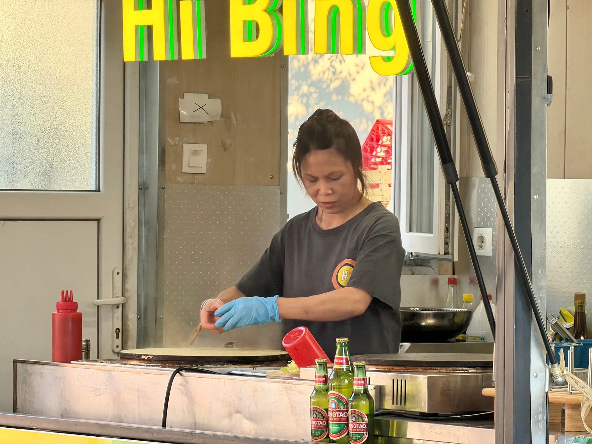 Chinese bing pancake being made at Fully Night Market Budapest A cook spreading batter on a griddle at the Hi Bing stall at Fully Night Market, Tsingtao bottles in the foreground.