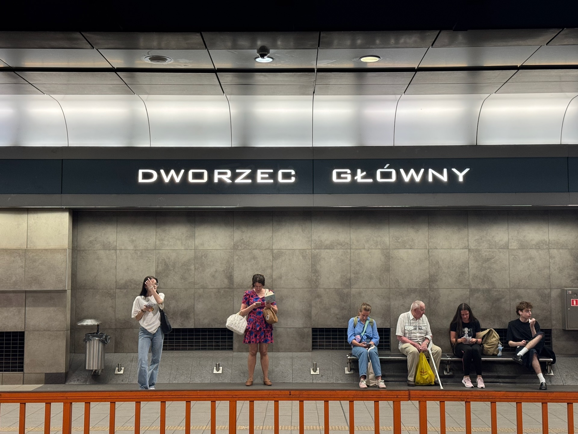 Passengers waiting on the underground platform at Kraków Główny station, marked "Dworzec Główny"