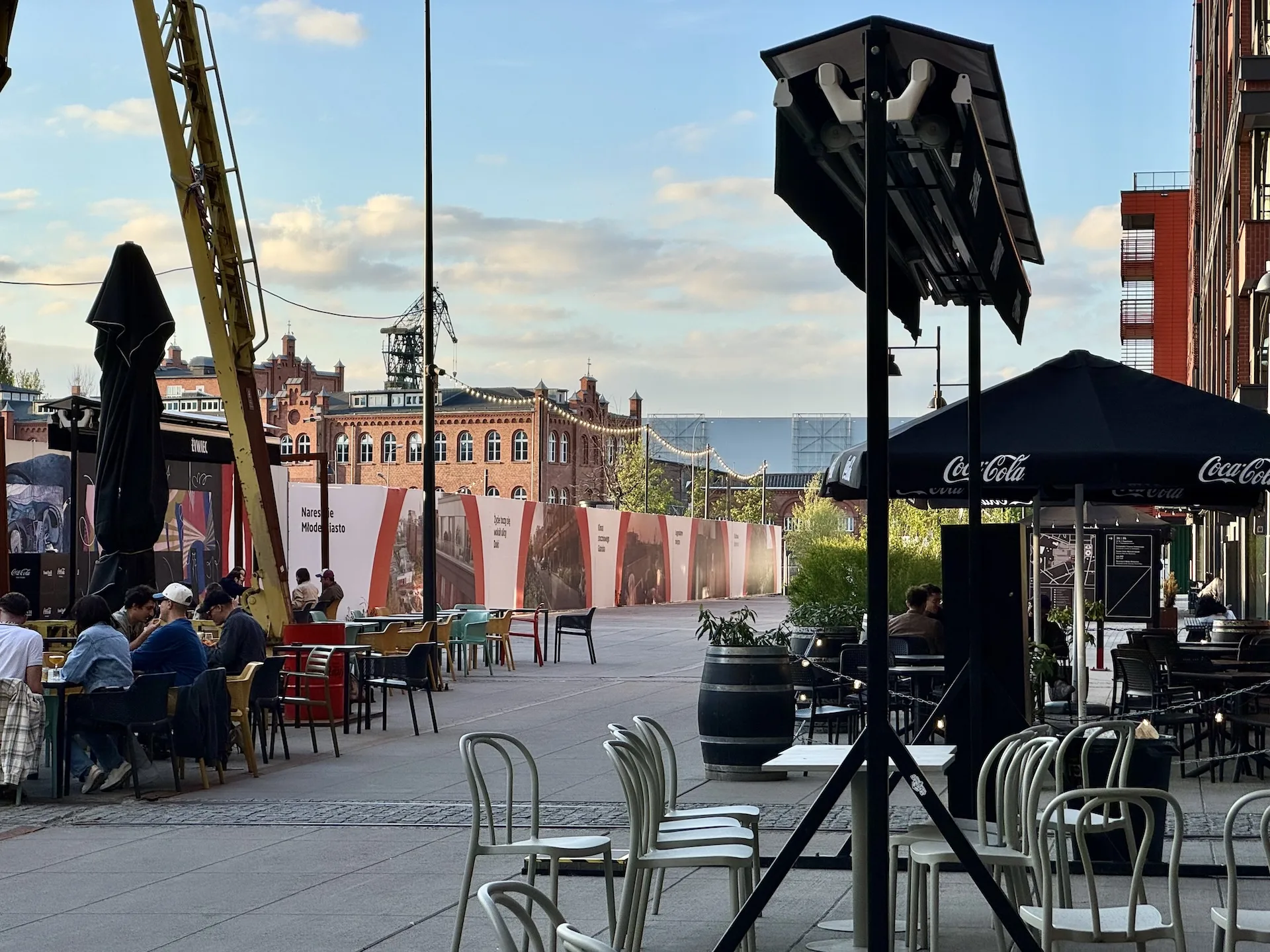 Outdoor tables at Montownia Food Hall in Gdańsk, a former German U-boat assembly hall, with a shipyard crane still standing outside.