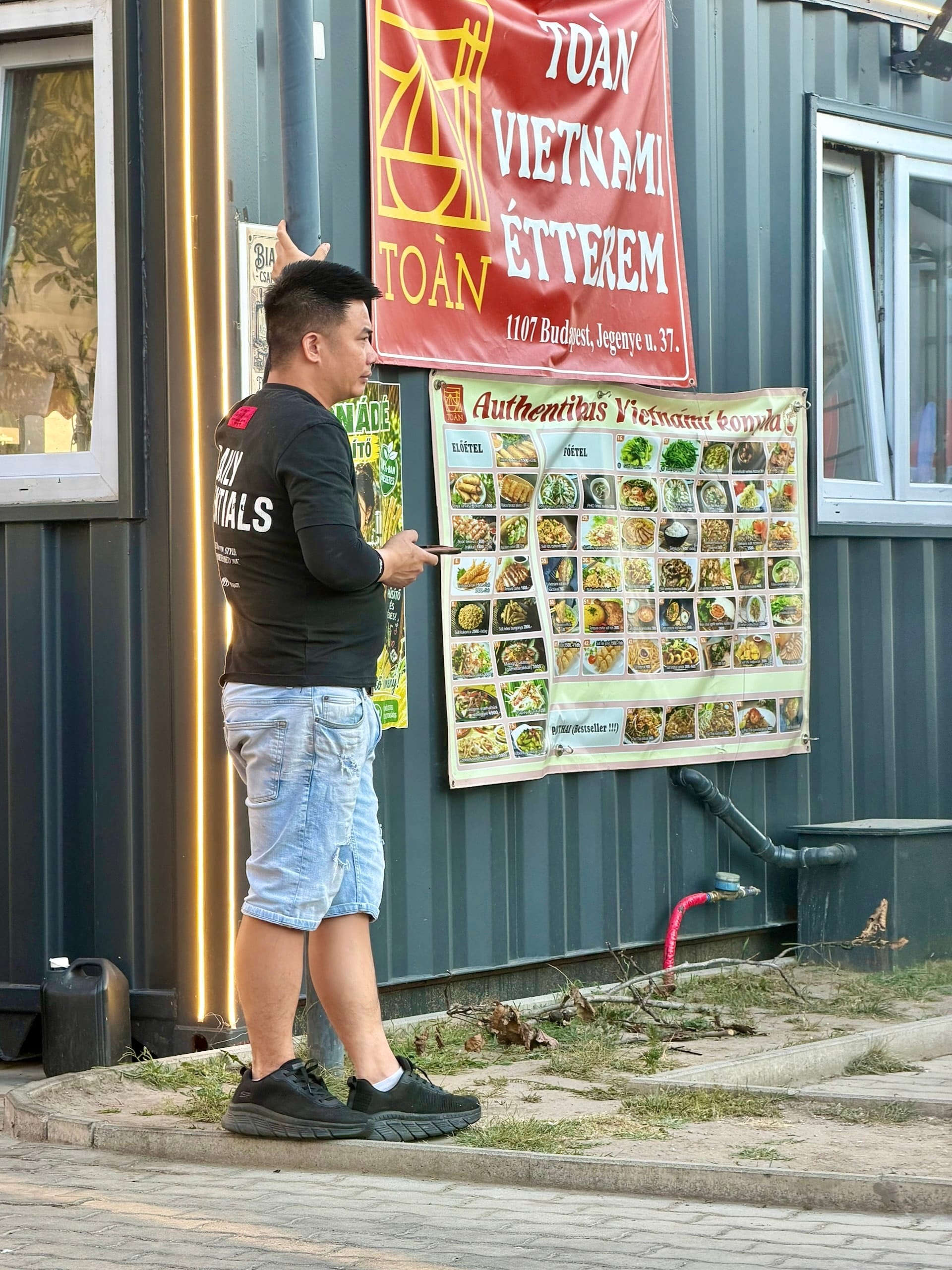 Toan Vietnamese restaurant stall at Fully Night Market Budapest A man outside the Toan Vietnamese restaurant stall at Fully Night Market, beside a photo menu of Vietnamese dishes.