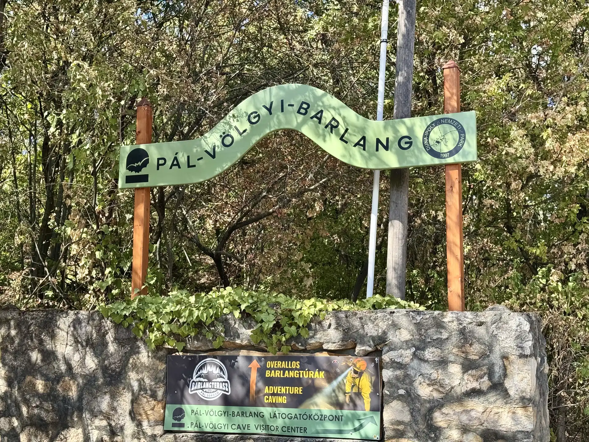 Pál-völgyi cave roadside entrance sign, Budapest Green Pál-völgyi-barlang sign at the roadside entrance, with an adventure caving banner on the wall below