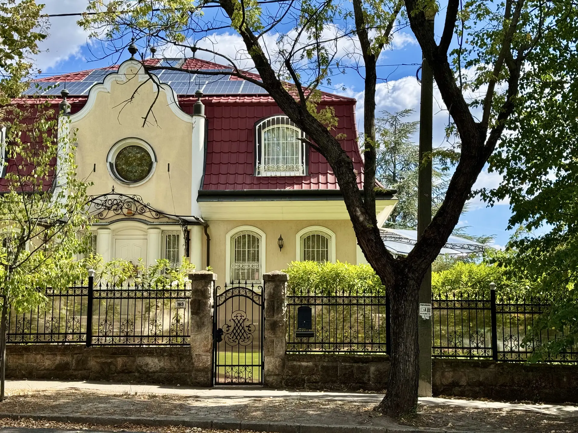 Villa on the walk between the Pál-völgyi and Szemlő-hegyi caves, Budapest Interwar villa with a red tiled roof and a round window, behind an iron fence on the walk between the two caves