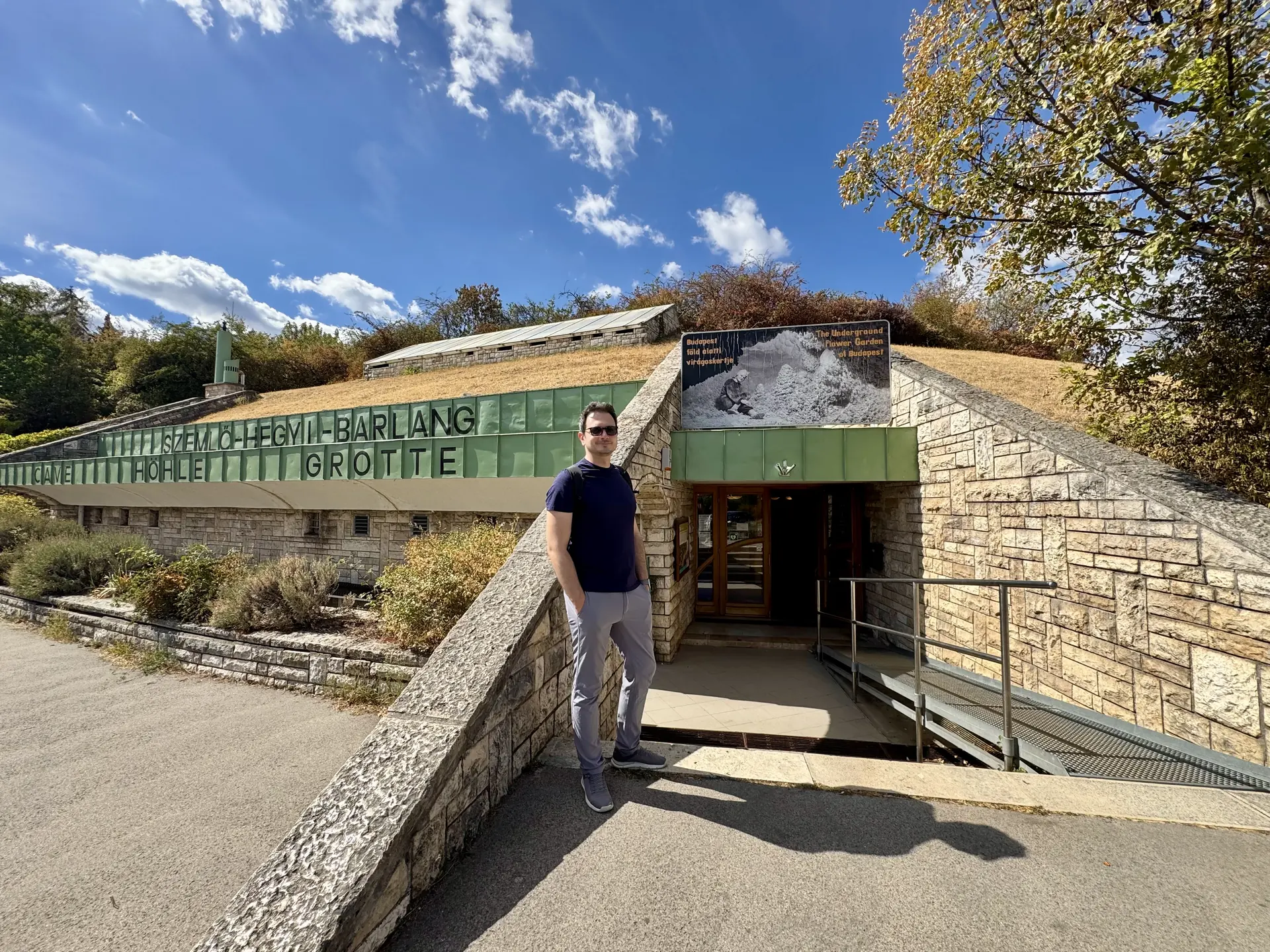 Szemlő-hegyi cave entrance building, Budapest Man standing at the entrance of the Szemlő-hegyi cave, with green lettering on the low visitor building and a ramp to the door