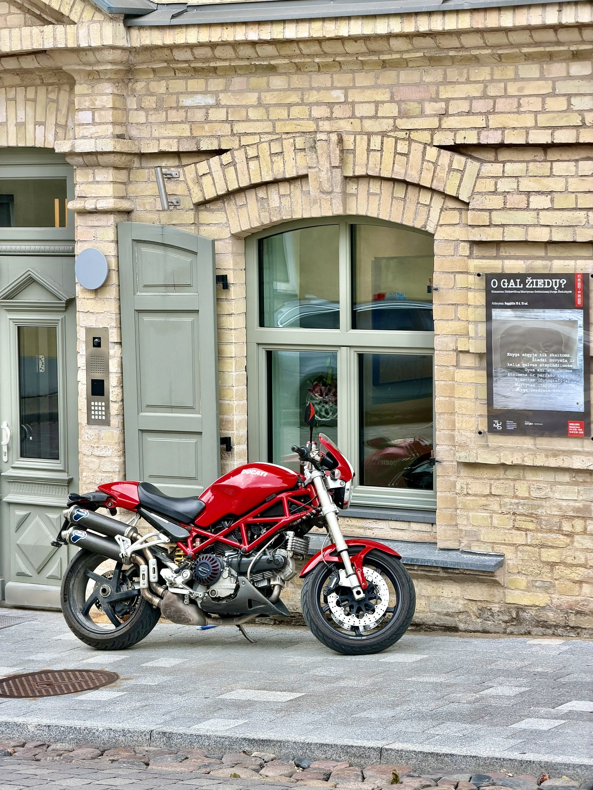 Ducati parked outside a building in Užupis A red Ducati Monster motorcycle parked against a yellow brick building in Užupis, Vilnius.