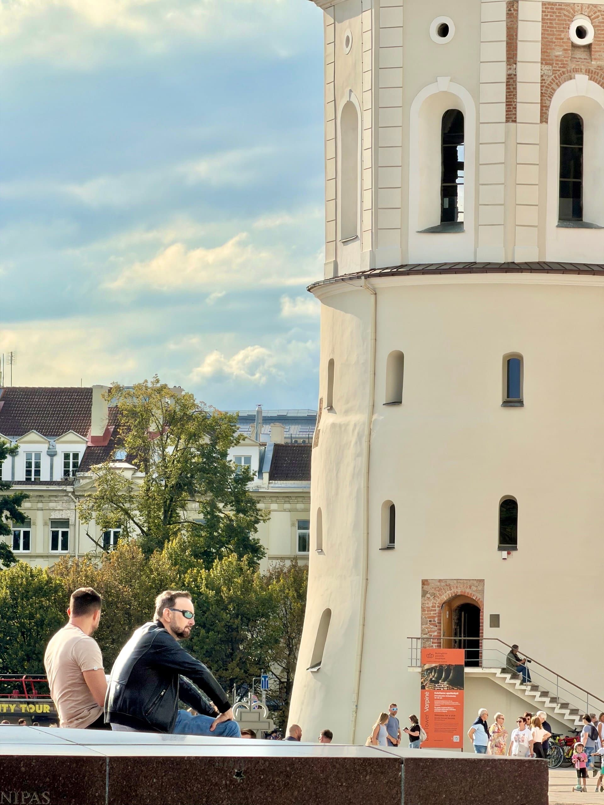 Free-standing bell tower of Vilnius Cathedral The white round lower stages of the free-standing bell tower of Vilnius Cathedral, with people sitting in front of it.