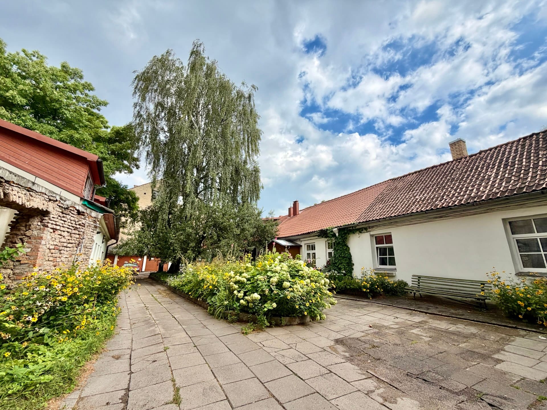 Inner courtyard in Vilnius Old Town A quiet courtyard in Vilnius with a low tiled-roof house, flowerbeds and a bench.