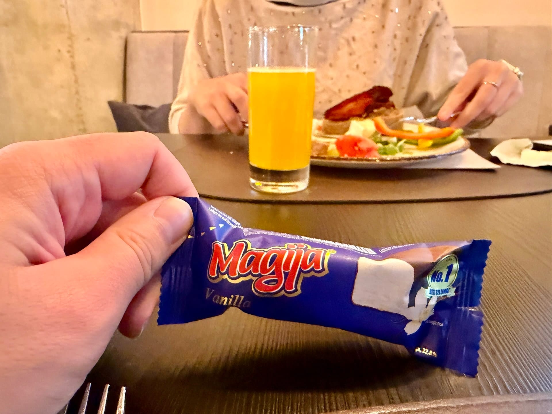 Magija glazed curd bar at a Vilnius hotel breakfast A hand holding a purple-wrapped Magija vanilla glazed curd bar at a hotel breakfast table in Vilnius.