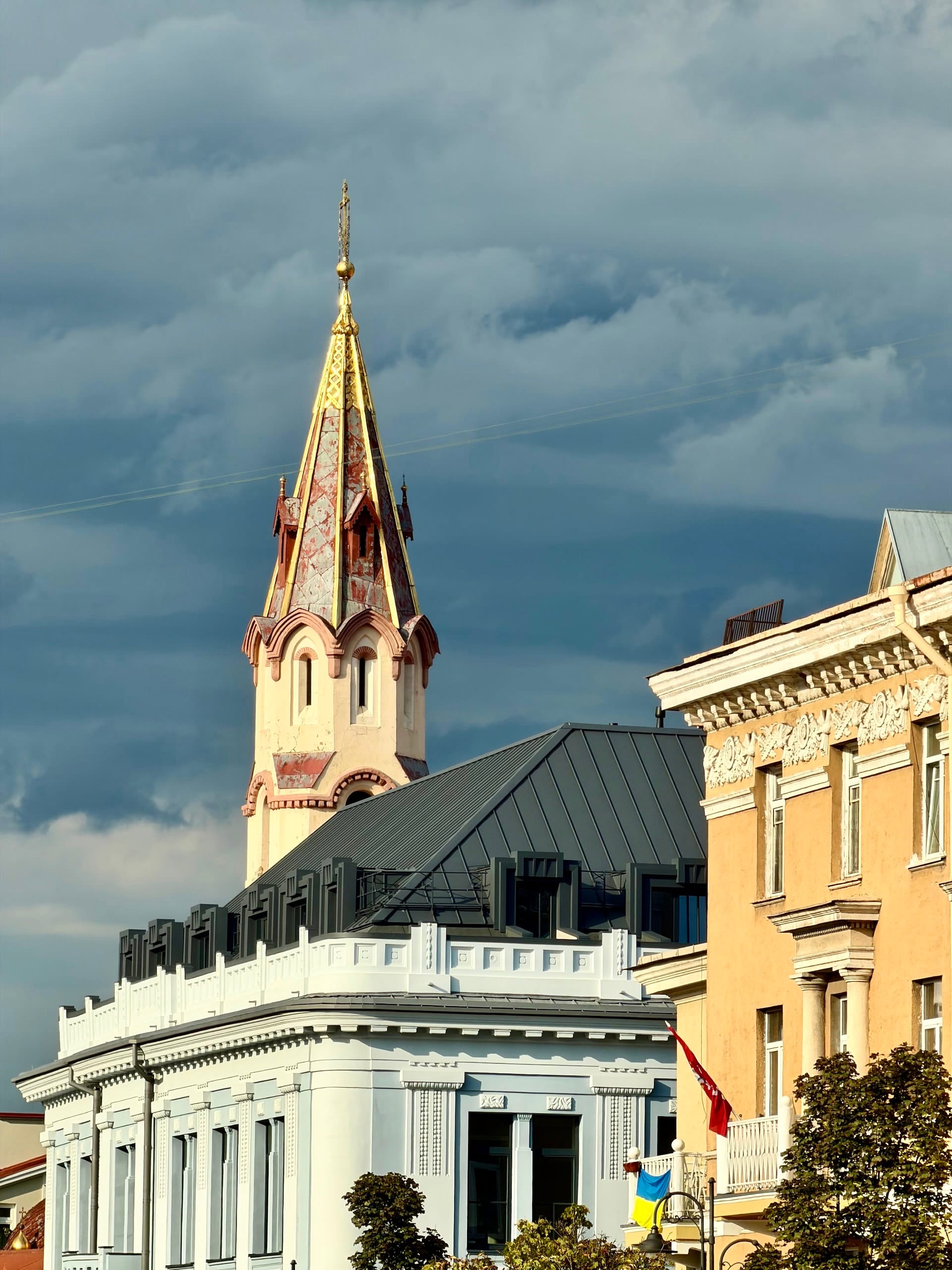 Storm clouds gathering over the rooftops of Vilnius A church spire with gilded ribs lit by low sun against heavy dark clouds over the rooftops of Vilnius.