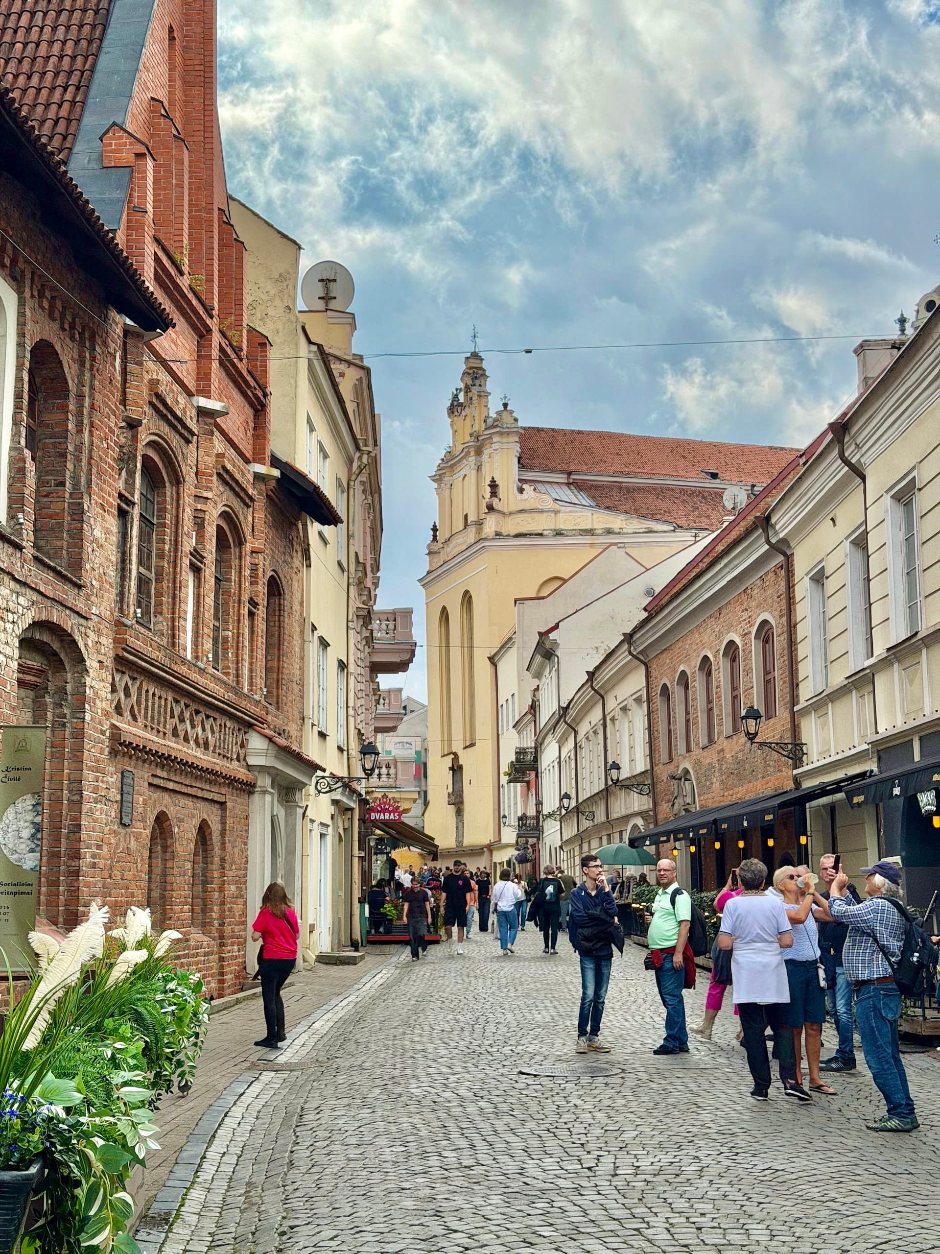 Street scene in Vilnius Old Town A cobbled street in Vilnius Old Town lined with brick and pastel buildings, people walking and photographing.