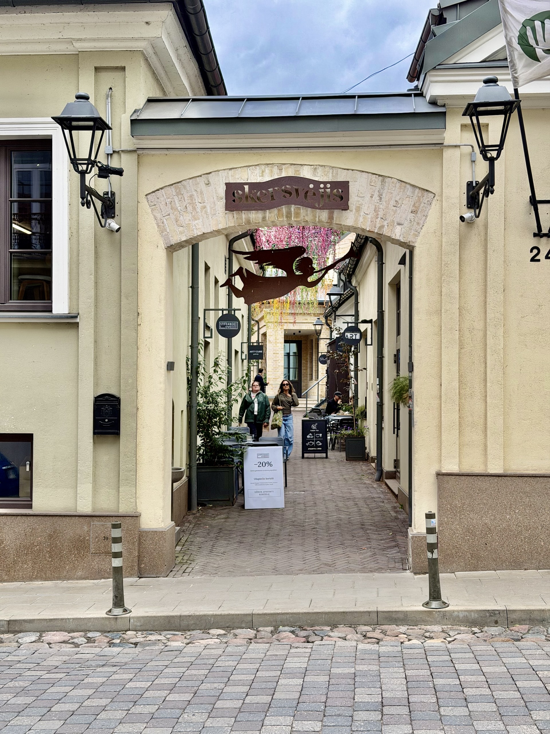 The Skersvėjis courtyard at Užupio 24 in Vilnius The restored Skersvėjis courtyard passage at Užupio 24 in Vilnius, a metal angel silhouette hanging in the archway.