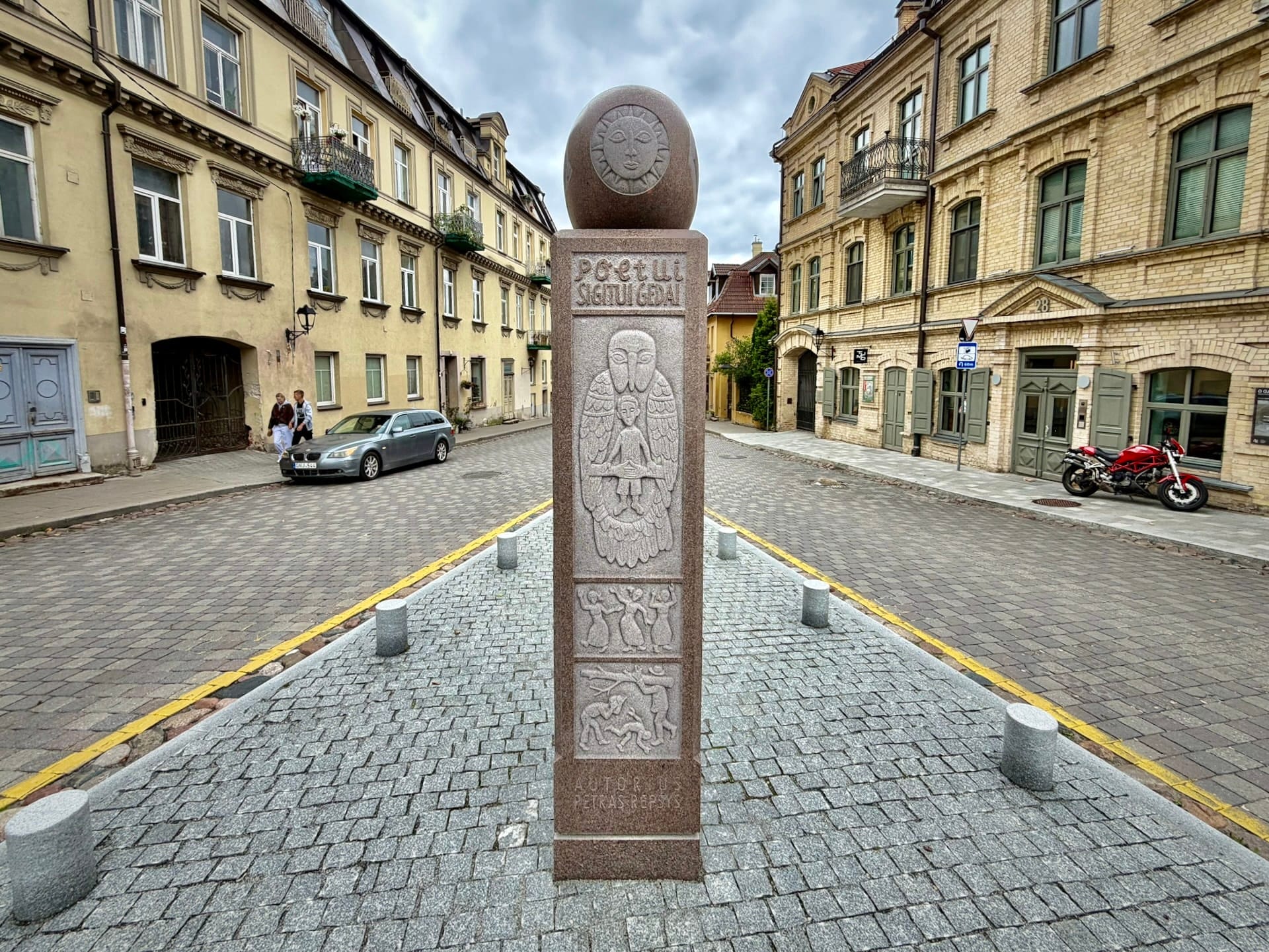 Užupis Obelisk to the poet Sigitas Geda The granite Užupis Obelisk standing in the roadway at the corner of Užupio and Krivių streets, carved with an angel and topped by a sun face.