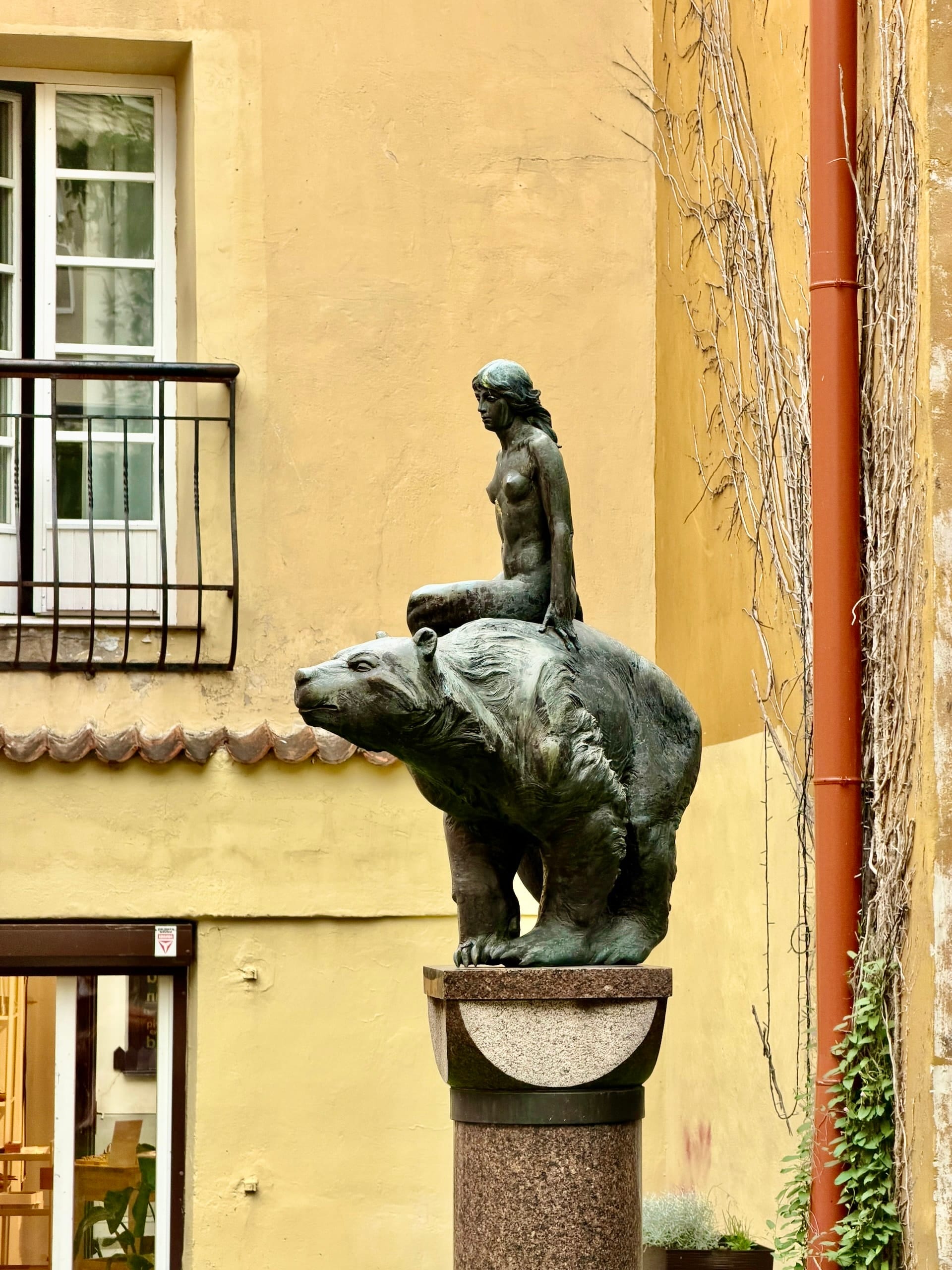 Woman riding a bear sculpture in a Vilnius courtyard Bronze sculpture of a half-naked woman riding a bear, on a granite column in a courtyard in Vilnius Old Town.