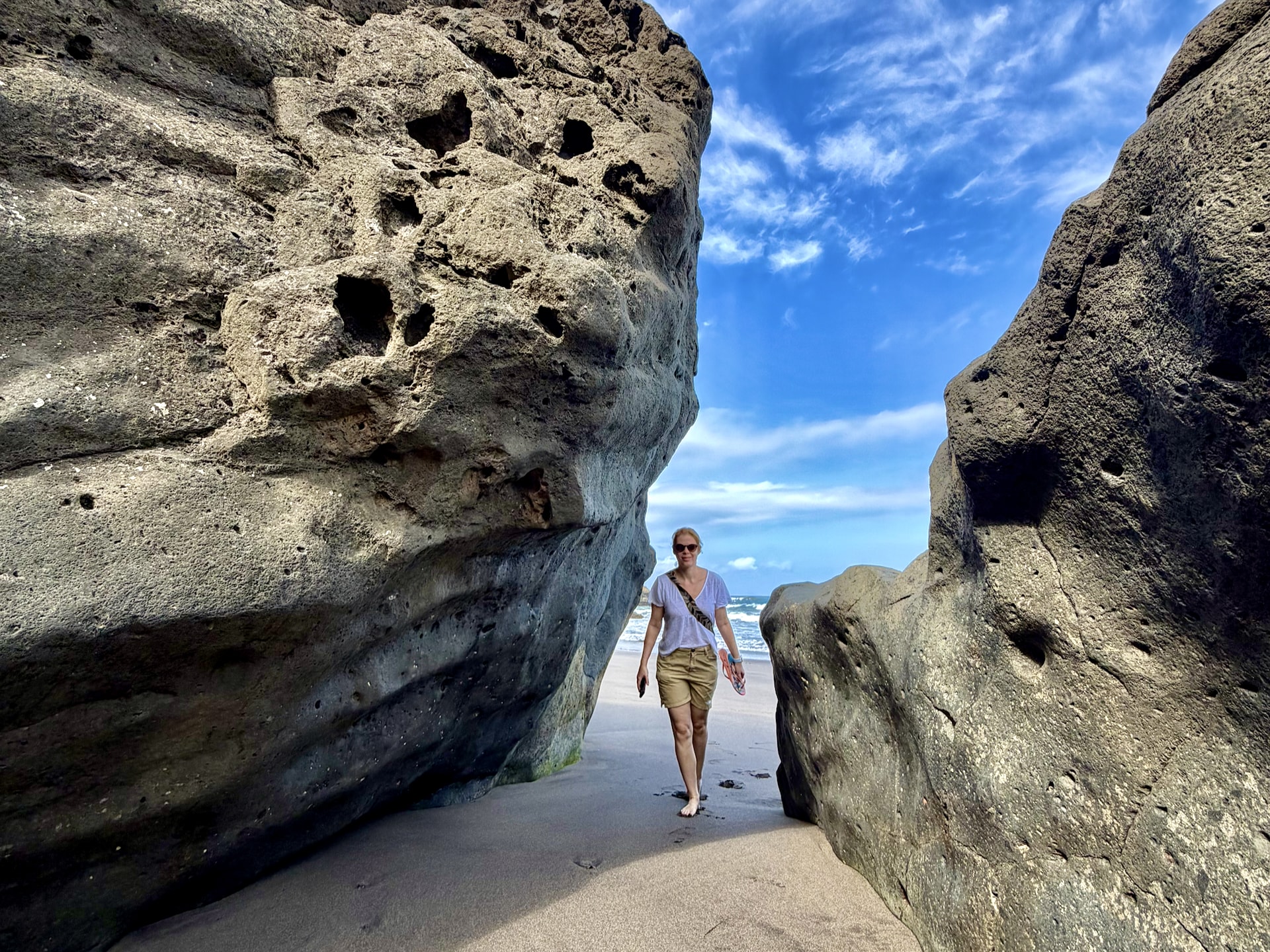 Andrea between giant boulders at Roque de las Bodegas Andrea walking barefoot on the sand between two huge weathered volcanic boulders at Roque de las Bodegas beach