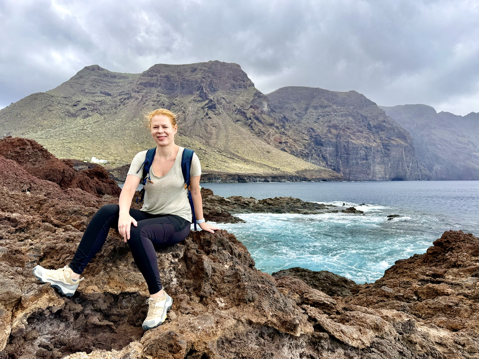 Andrea sitting on volcanic rocks at Punta de Teno, with waves and the Teno cliffs behind her