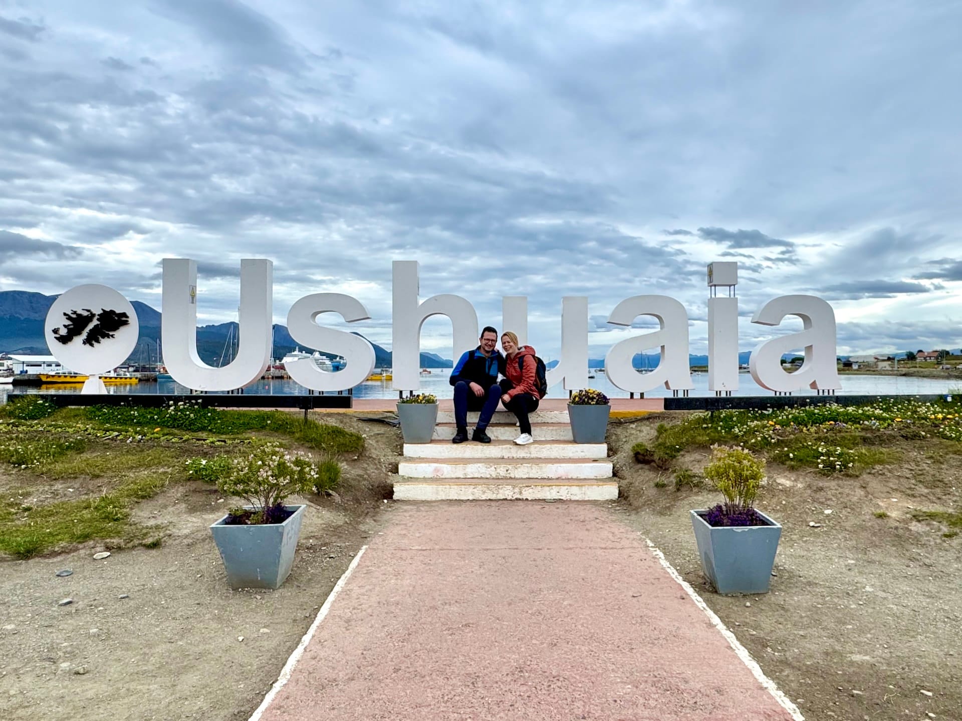 Laszlo and Andrea sitting on the big white USHUAIA letters with the Malvinas islands outline on the waterfront