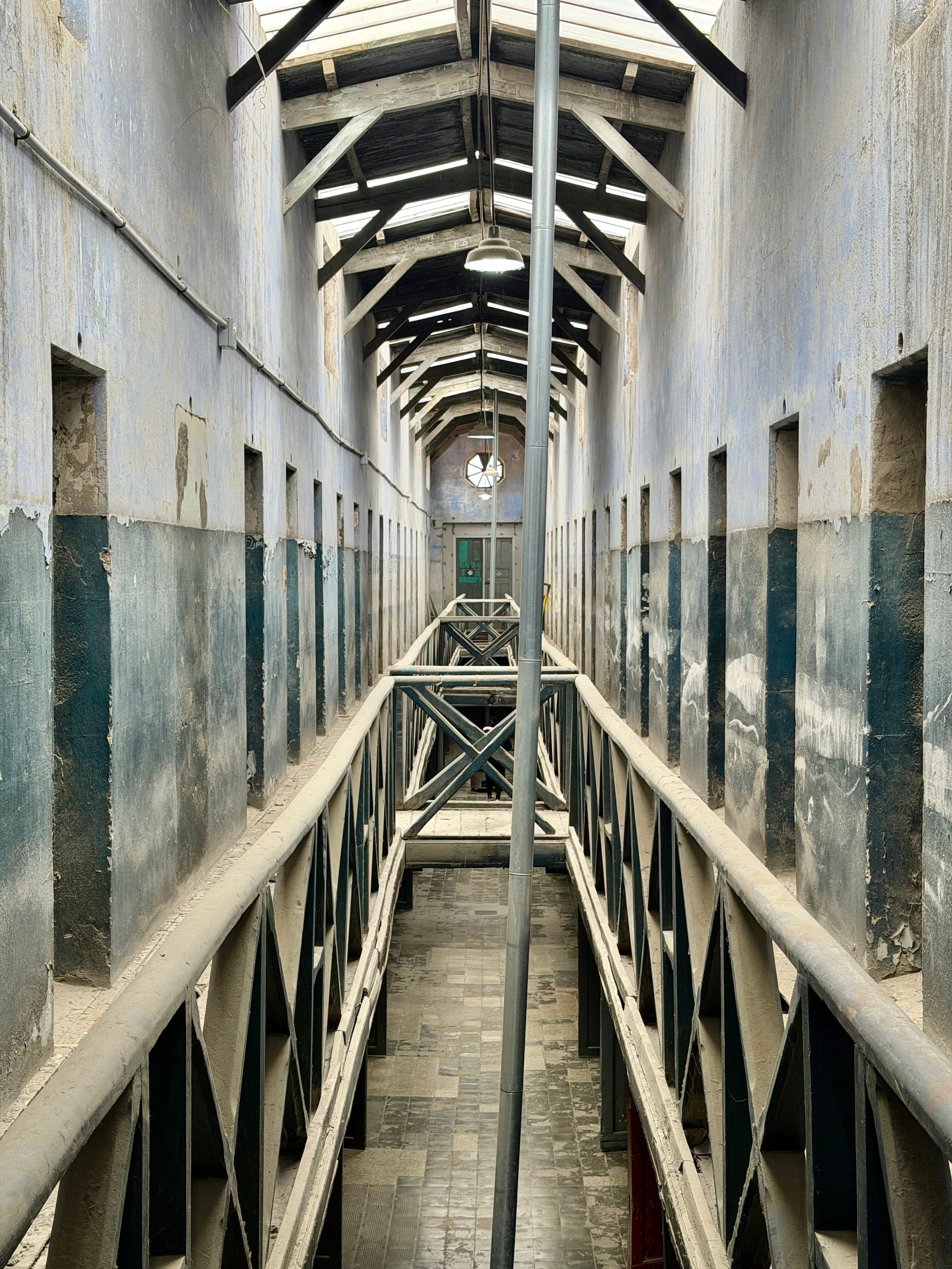 Long cellblock in the old Ushuaia prison with tiny cell doors on both sides and an iron walkway down the middle
