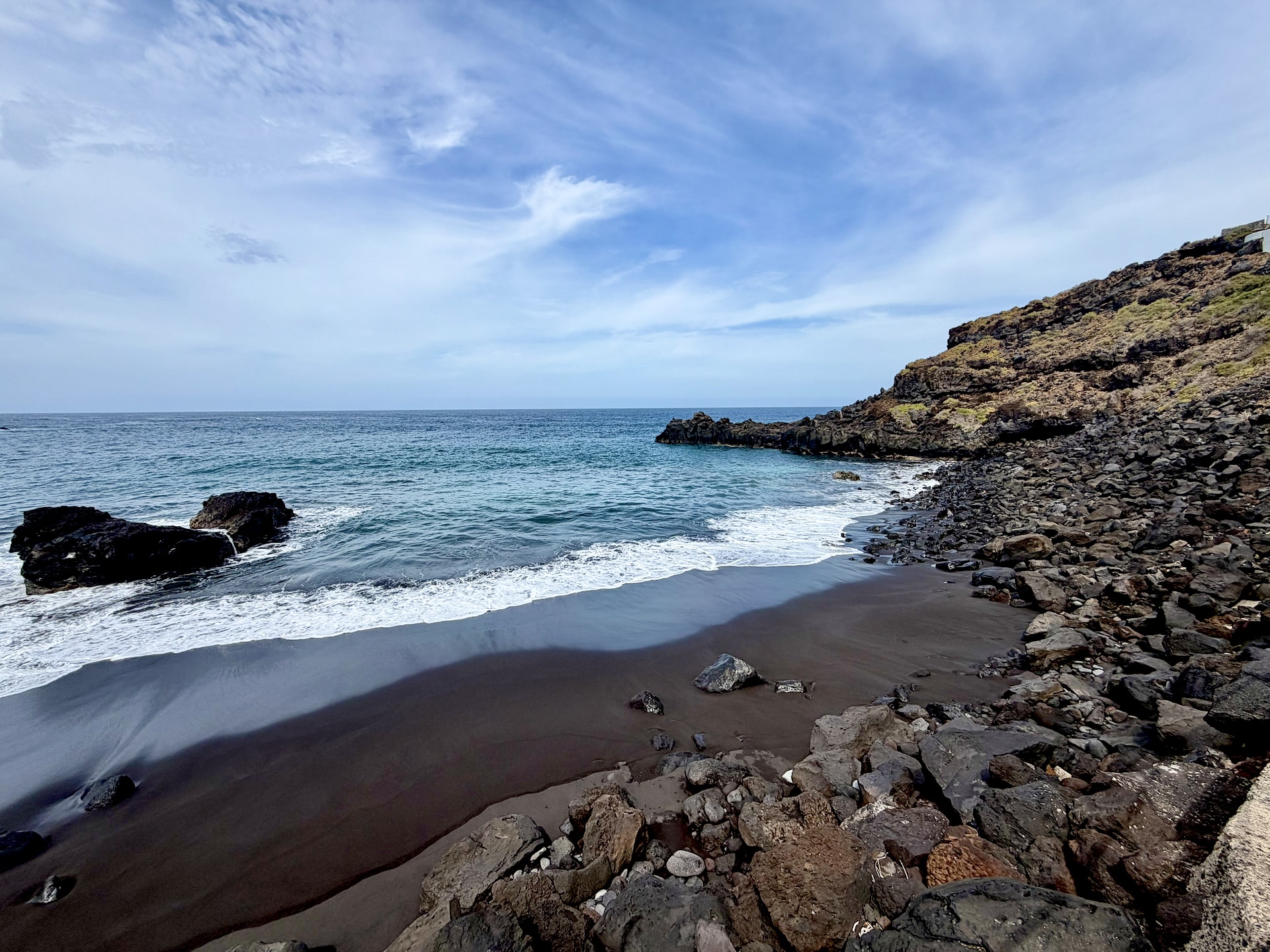 Closed-off cove at El Bollullo beach, Tenerife Small black sand cove beside El Bollullo, hemmed in by boulders and a rocky headland, with waves rolling in