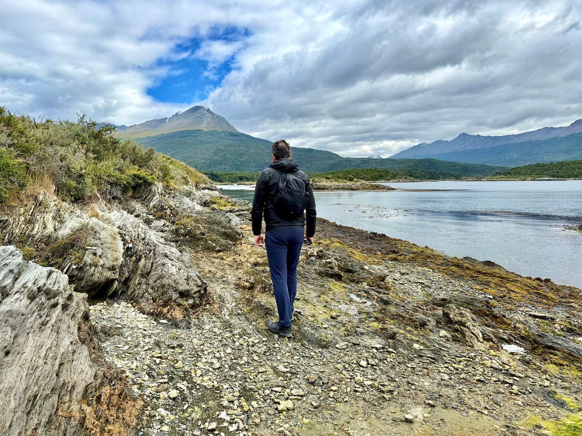 Laszlo walking a rocky coastal trail near Bahía Lapataia with mountains across the bay