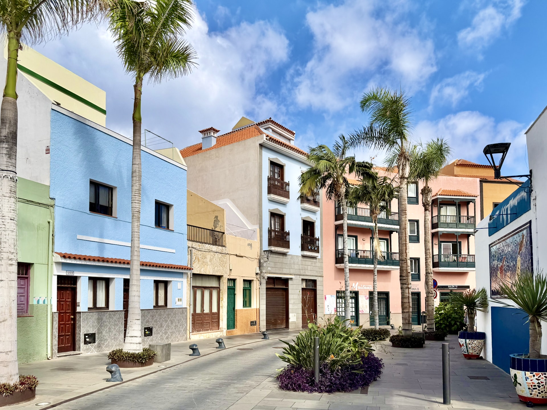 Pastel blue, cream and pink houses with wooden balconies and palm trees on Calle Mequínez in La Ranilla, Puerto de la Cruz