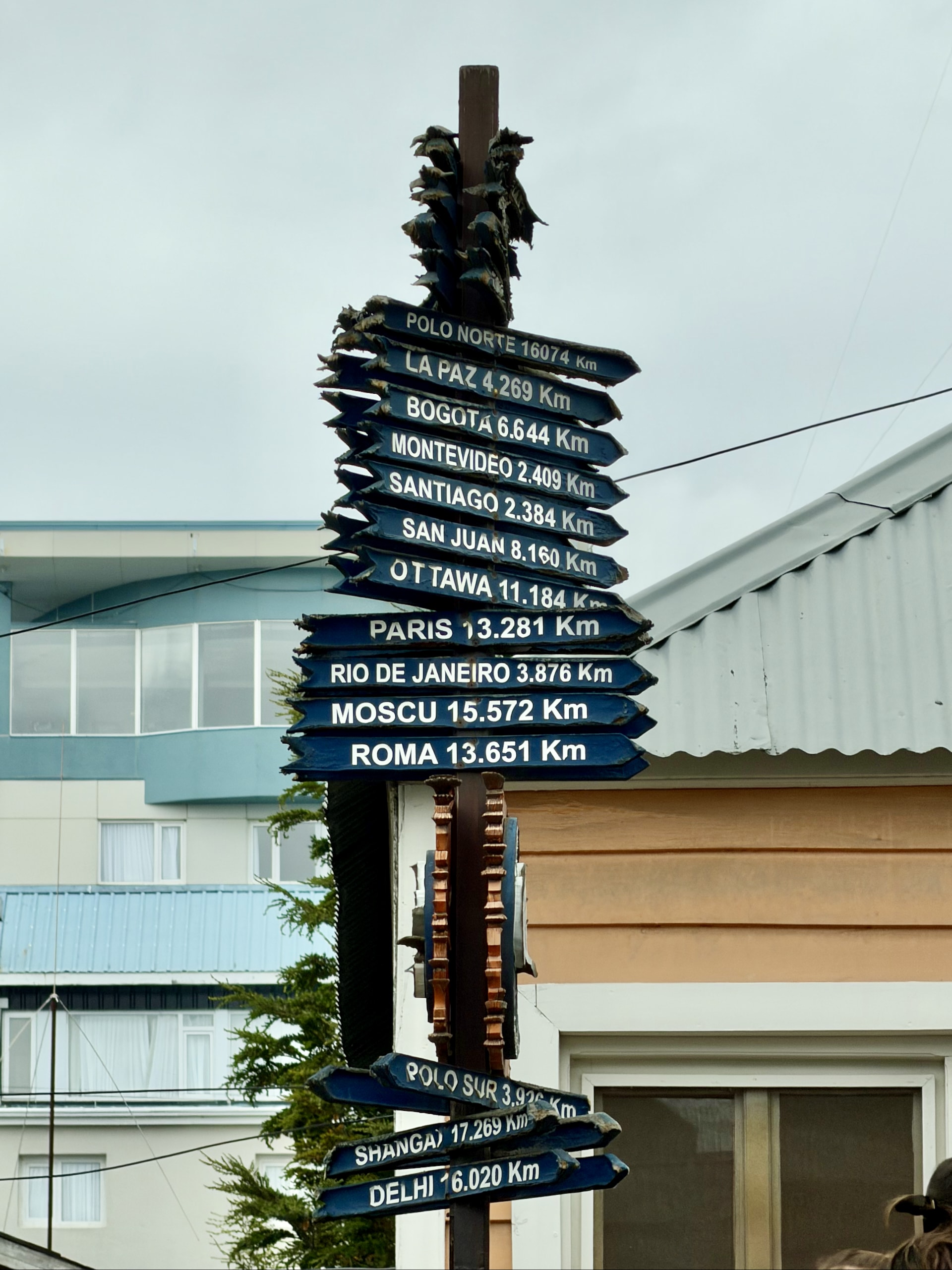 Signpost by Bodegón Fueguino listing distances from Ushuaia to the North Pole, Paris, Moscow, Rome and other places