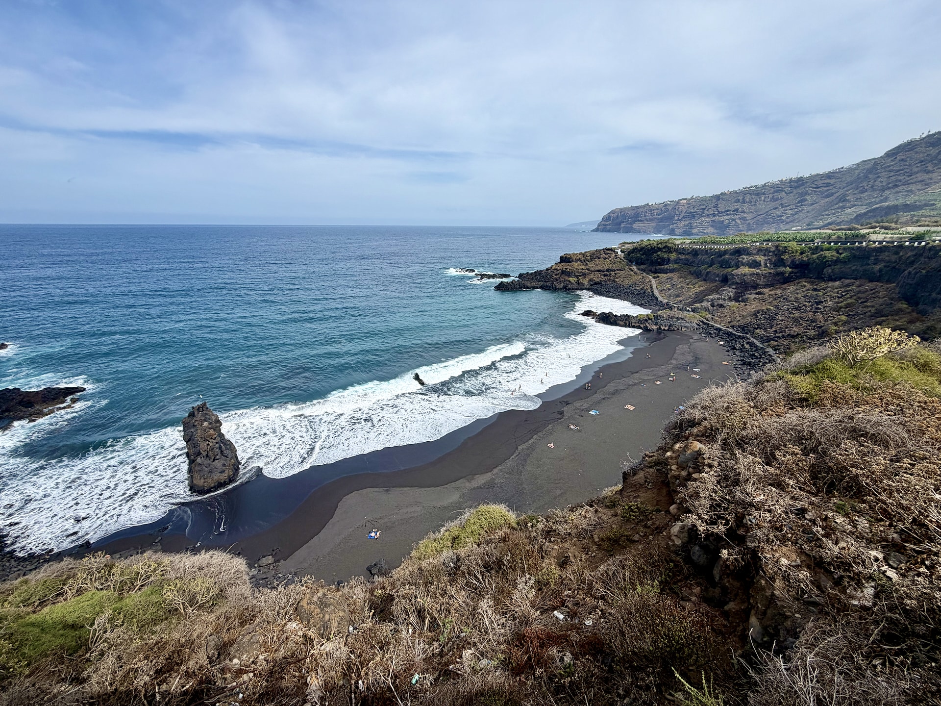 El Bollullo black sand beach from above, La Orotava El Bollullo's black sand cove from the cliff path, with a sea stack in the surf and only a handful of people on the beach