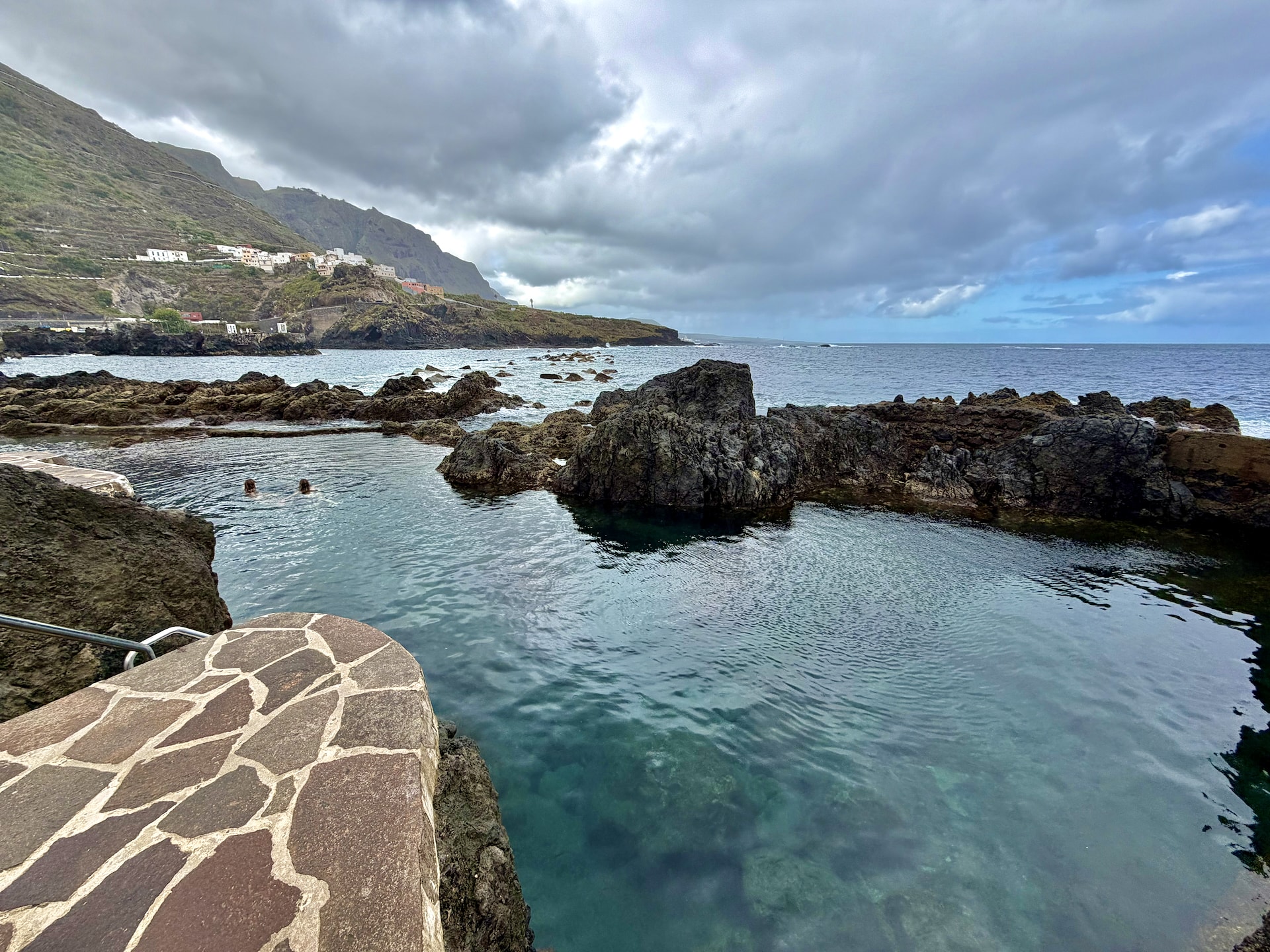 El Caletón natural pools in Garachico on a cloudy day El Caletón natural rock pools in Garachico under gray clouds, two swimmers in clear water between black lava rocks