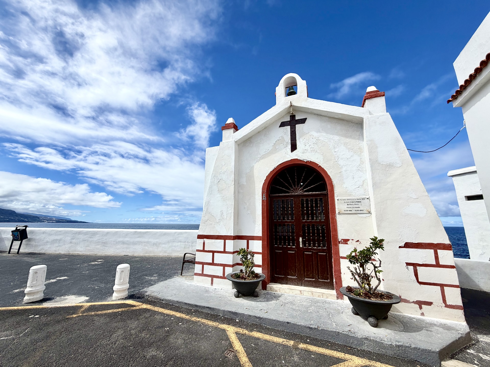 Small whitewashed chapel with a bell gable, a cross and red trim beside the sea at the end of a street in Punta Brava, Puerto de la Cruz