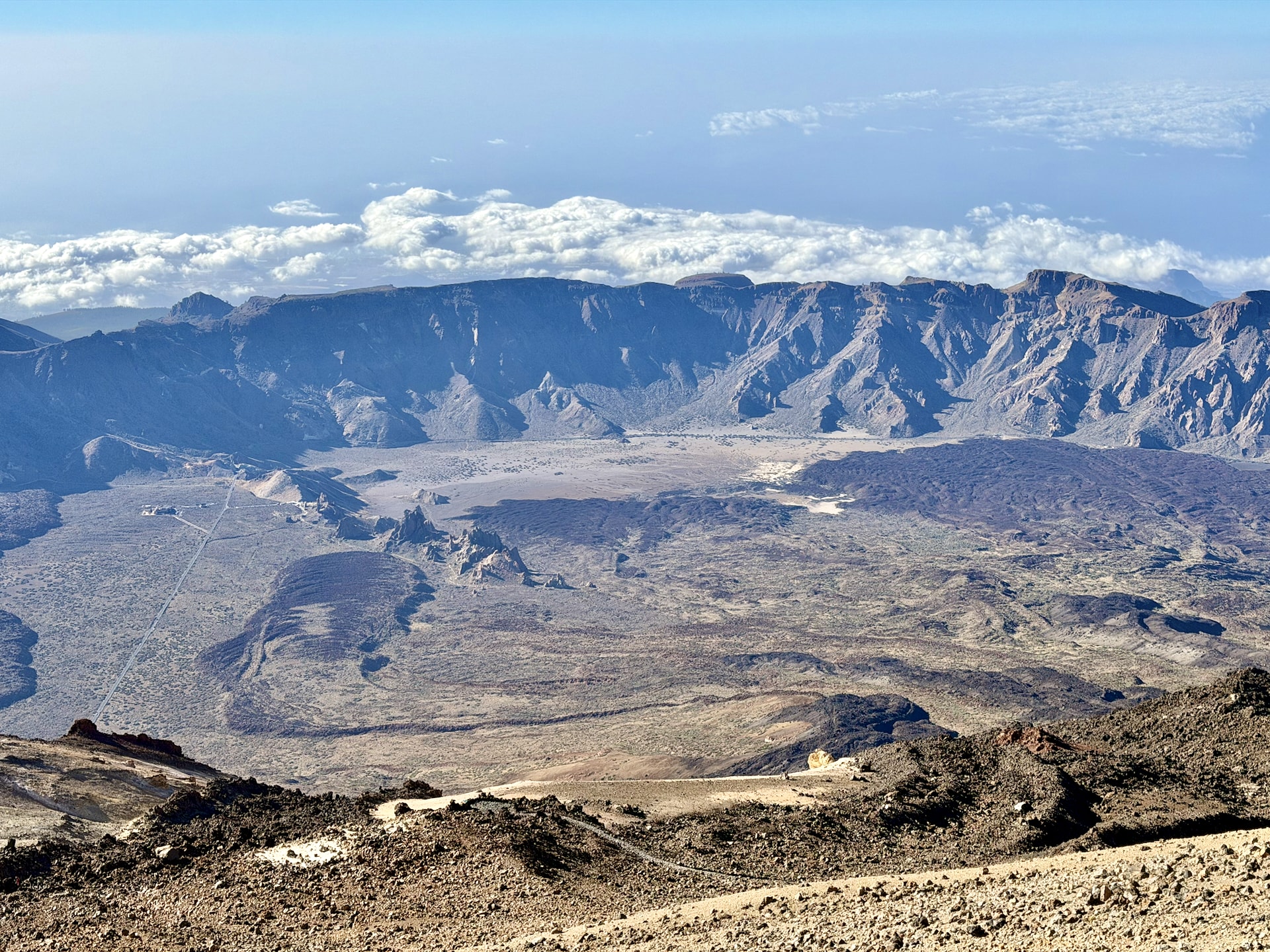 The Las Cañadas caldera seen from high on Mount Teide, its long rock wall stretching across the frame with clouds and the sea beyond