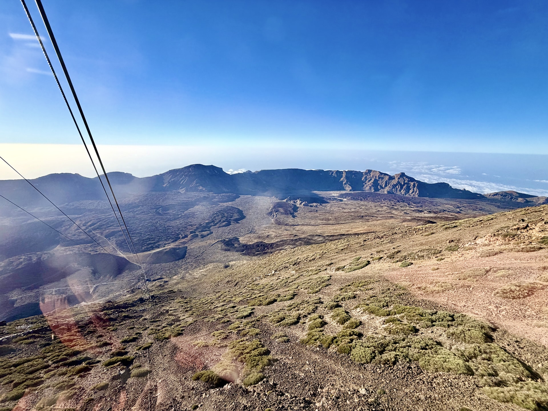 The Las Cañadas caldera seen through the window of the Teide cable car, with the cables running down the slope and the caldera wall in the distance