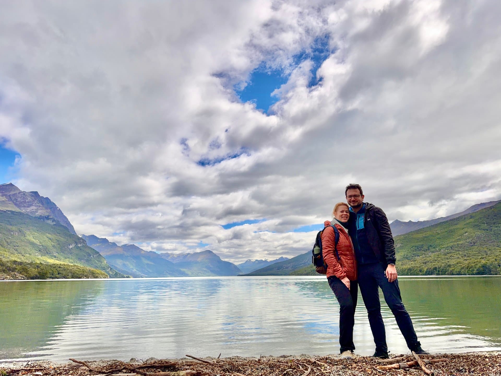 Laszlo and Andrea standing on the pebble shore of Lago Roca with mountains and clouds behind
