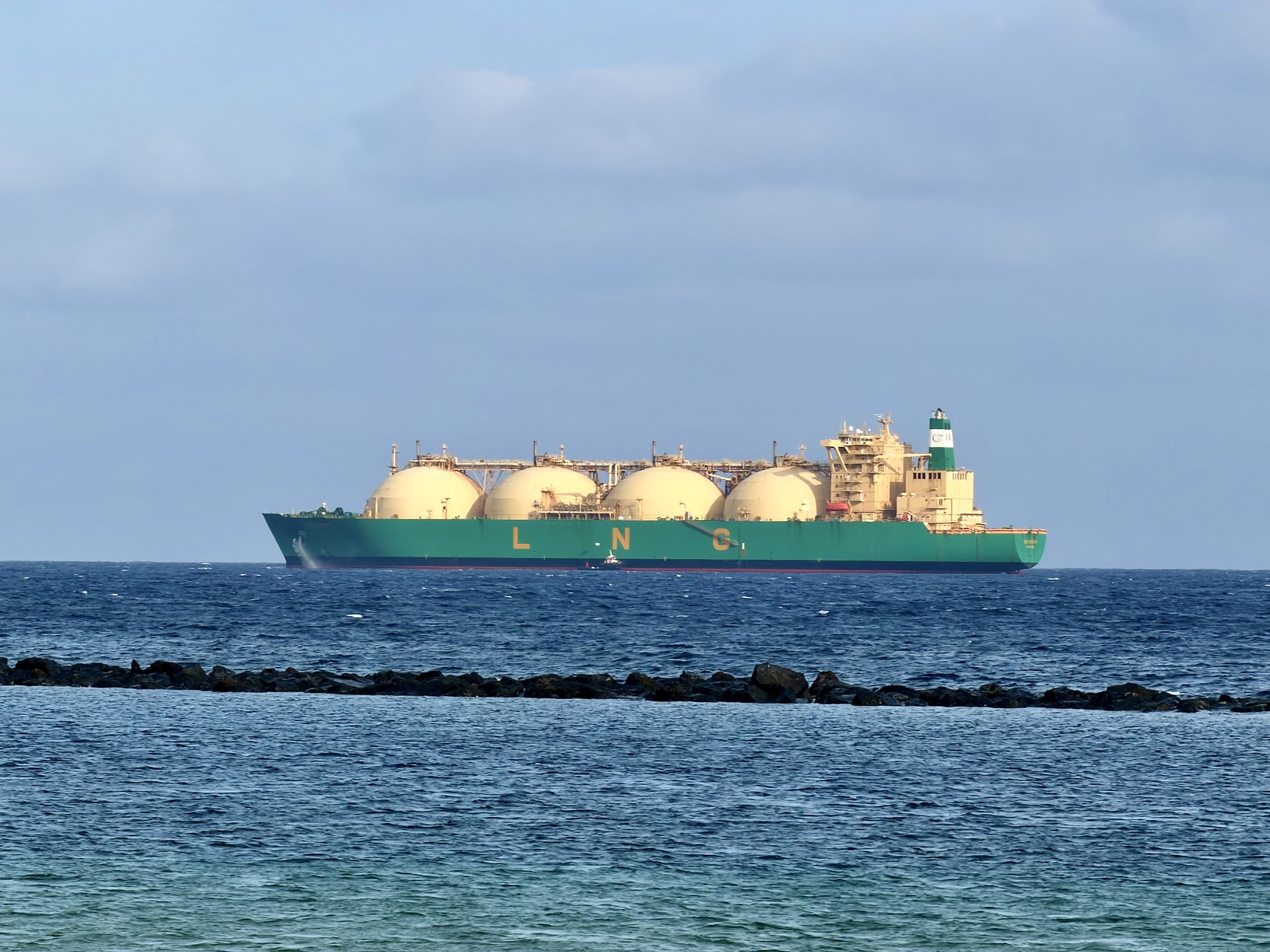 Green LNG tanker with four spherical tanks anchored offshore beyond the dark breakwater at Playa de Las Teresitas