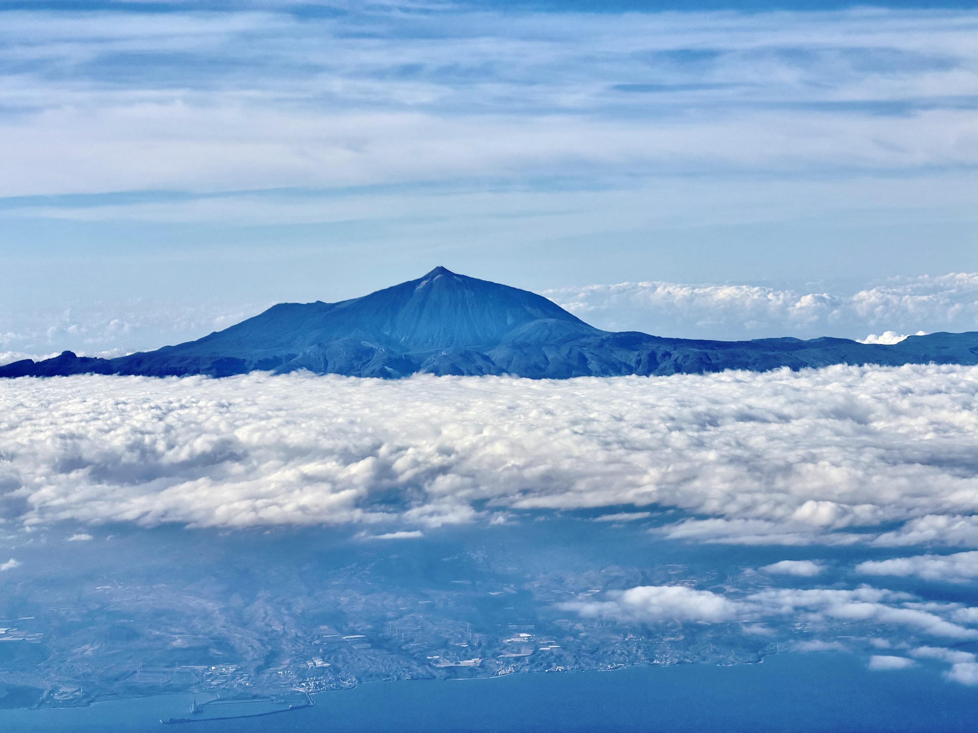 Mount Teide rising above a sea of clouds over Tenerife, seen from a plane, with the island's coastline visible below