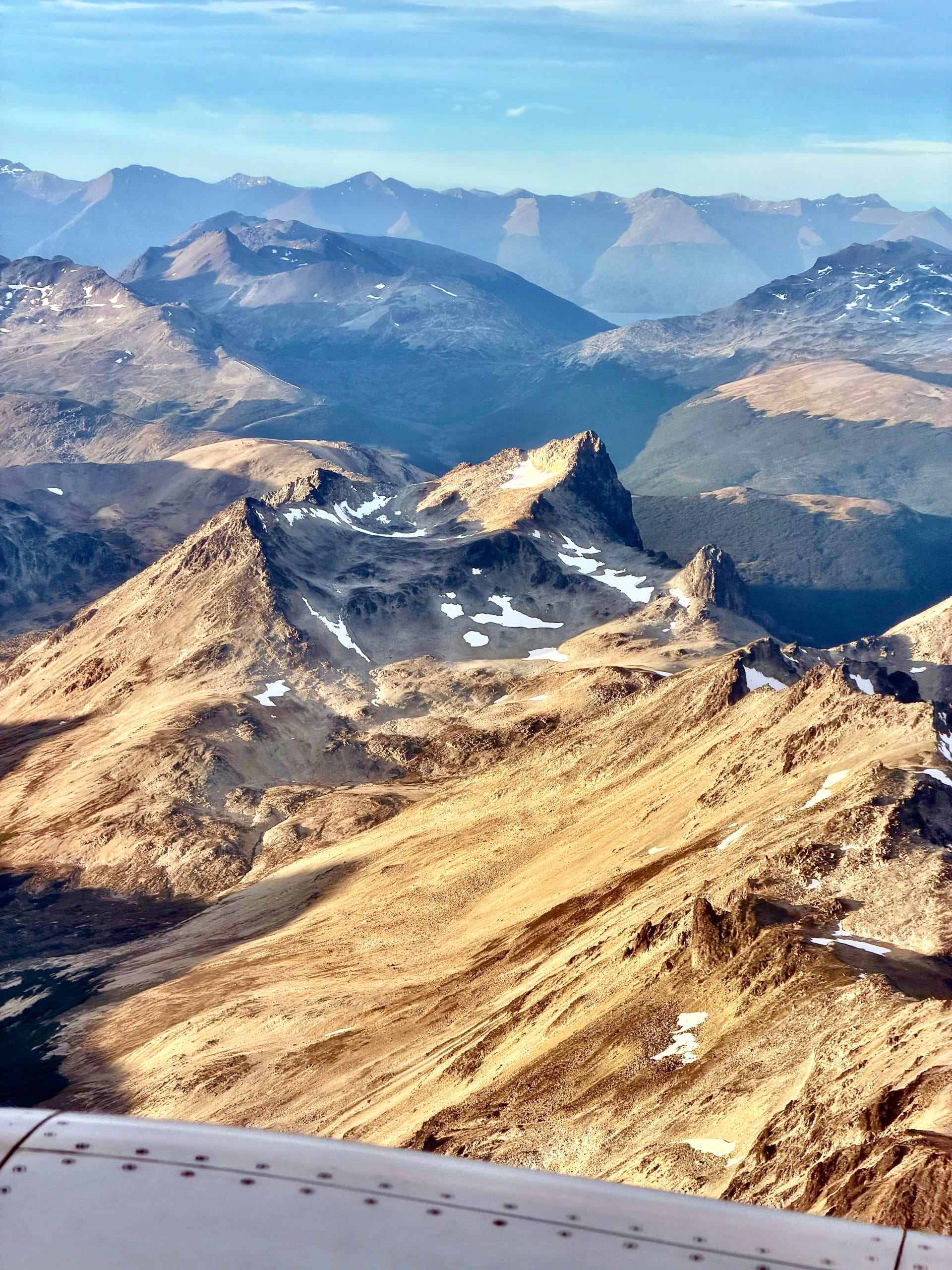 Rugged golden-brown mountain ridges just below the aircraft wing on the approach to Ushuaia