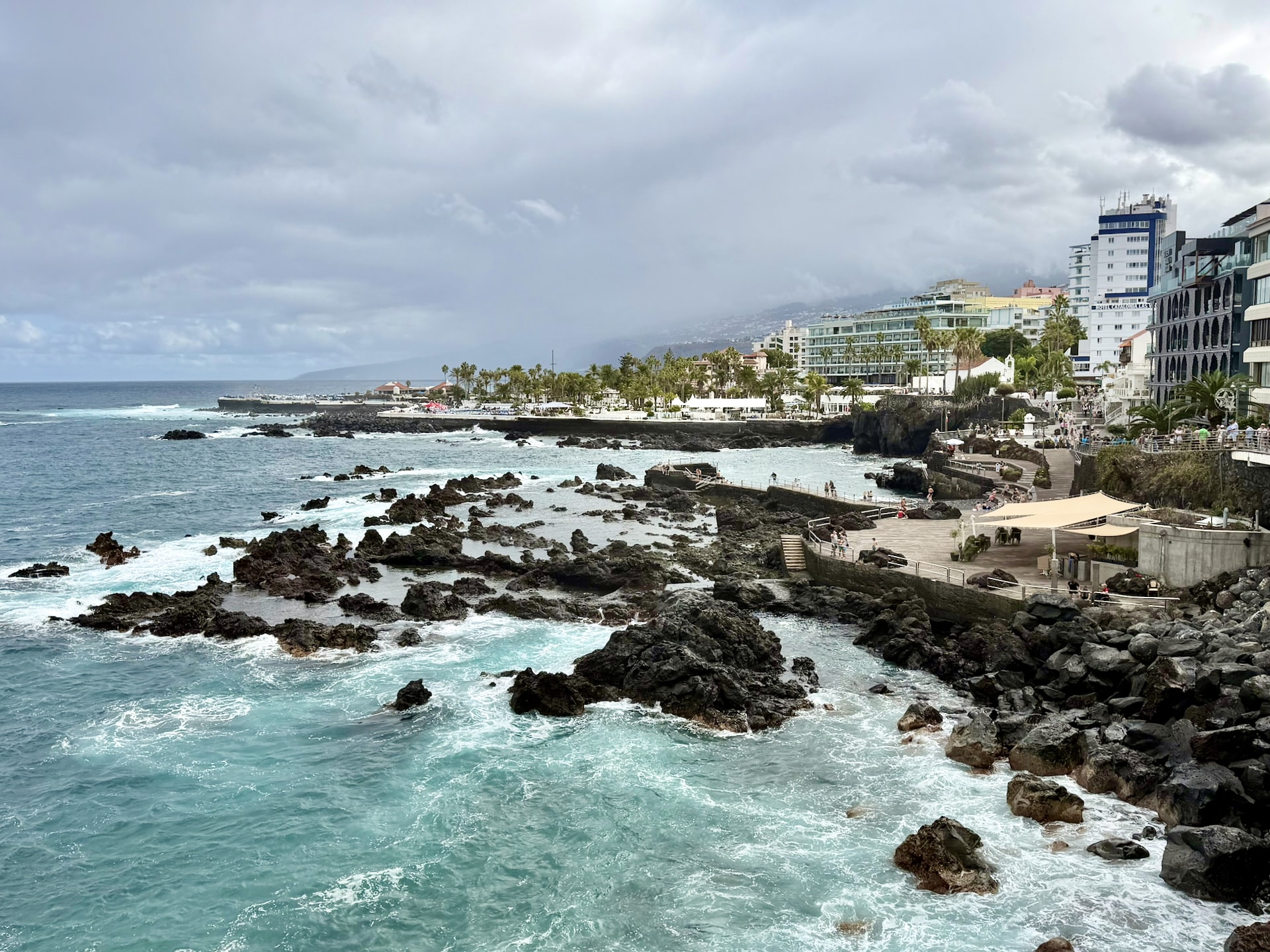 Natural pools and open sea on the Puerto de la Cruz seafront Rocky seafront of Puerto de la Cruz, with calm natural pools behind black lava rocks, rough open sea beyond and hotels along the shore